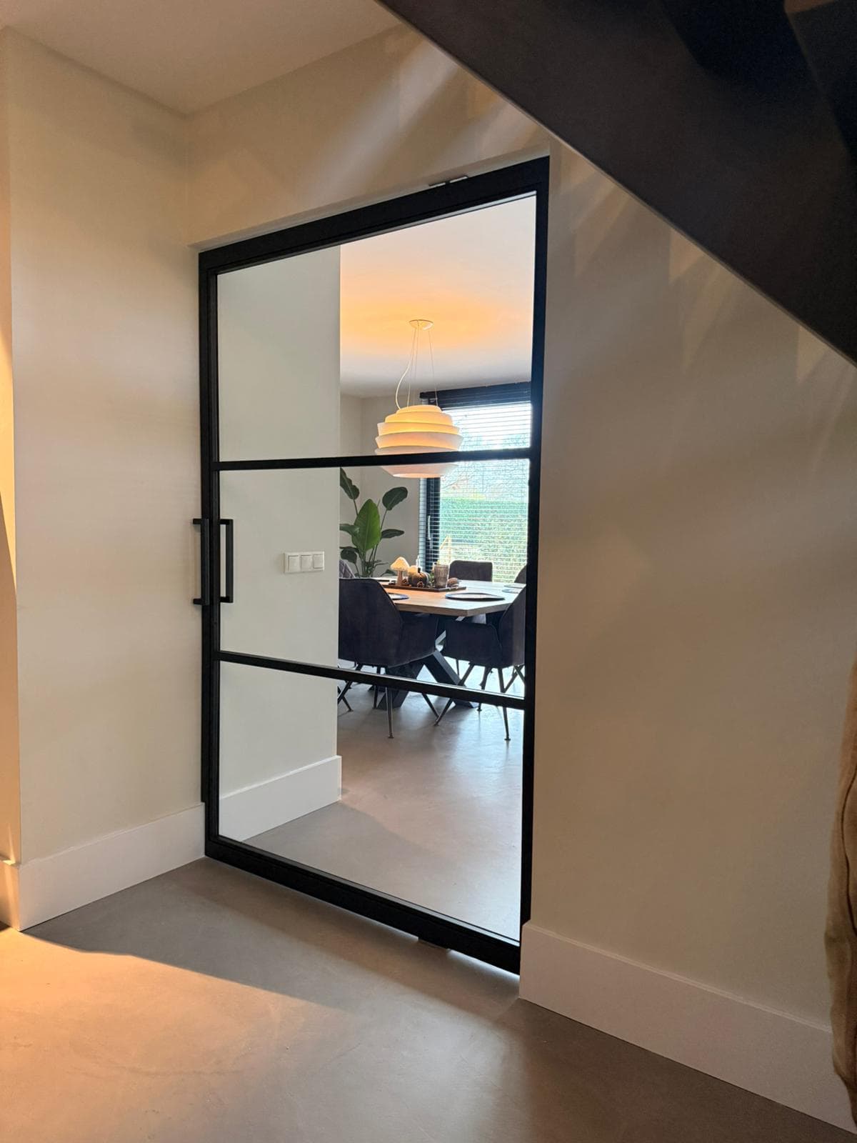 Brede stalen taatsdeur op maat met een moderne 3-vaks verdeling en helder glas tussen de hal en de lichte woonkeuken.