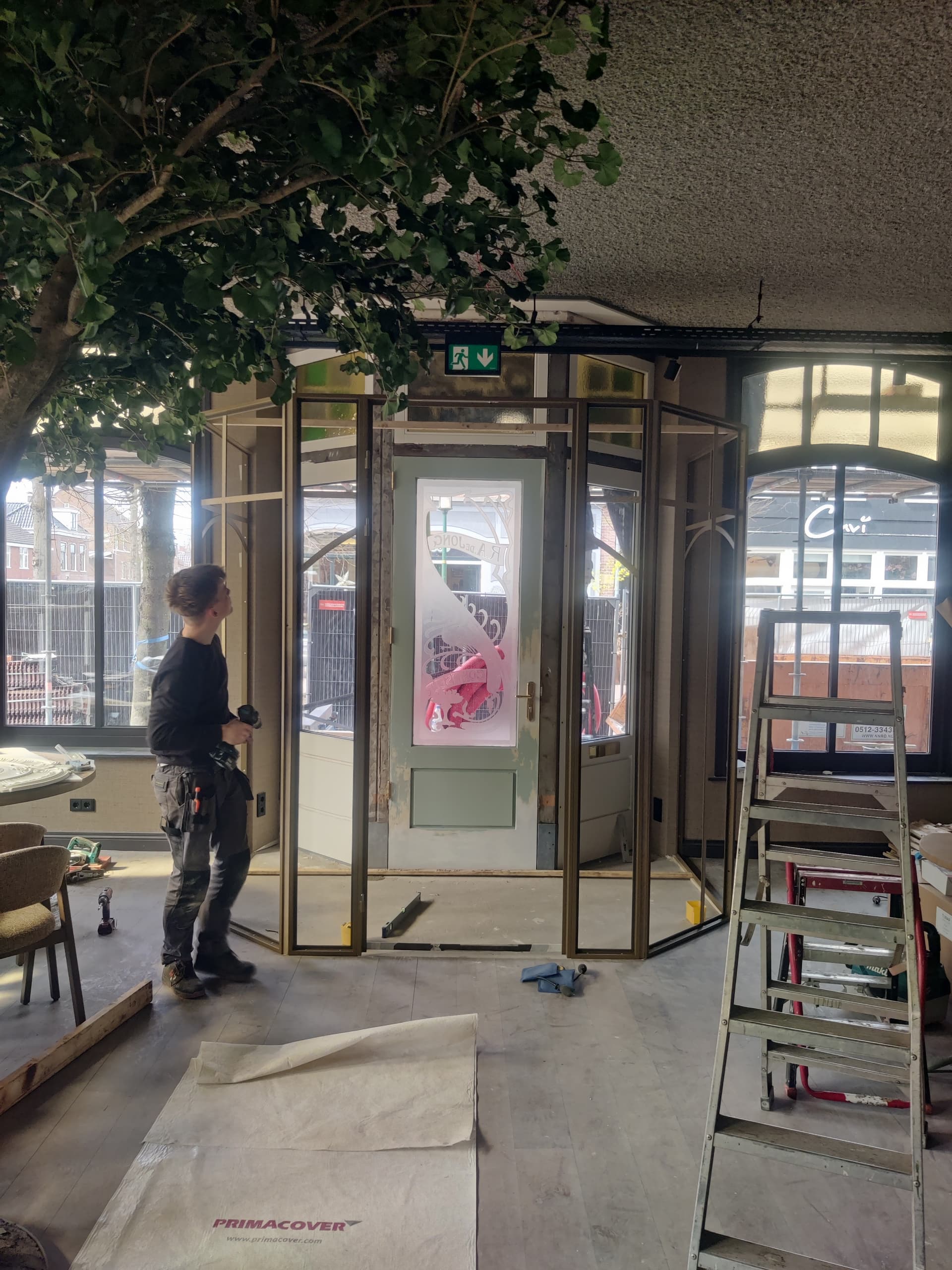 Montage van een goudkleurige stalen tochtsluis op maat rondom de café-entree om tocht in de horeca tegen te gaan.