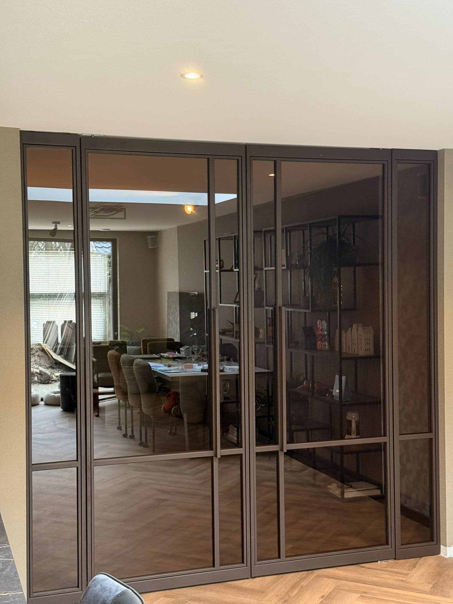 Kamerhoge bruine stalen pui met dubbele openslaande deuren, vaste zijpanelen en getint glas in een luxe interieur met visgraatvloer.