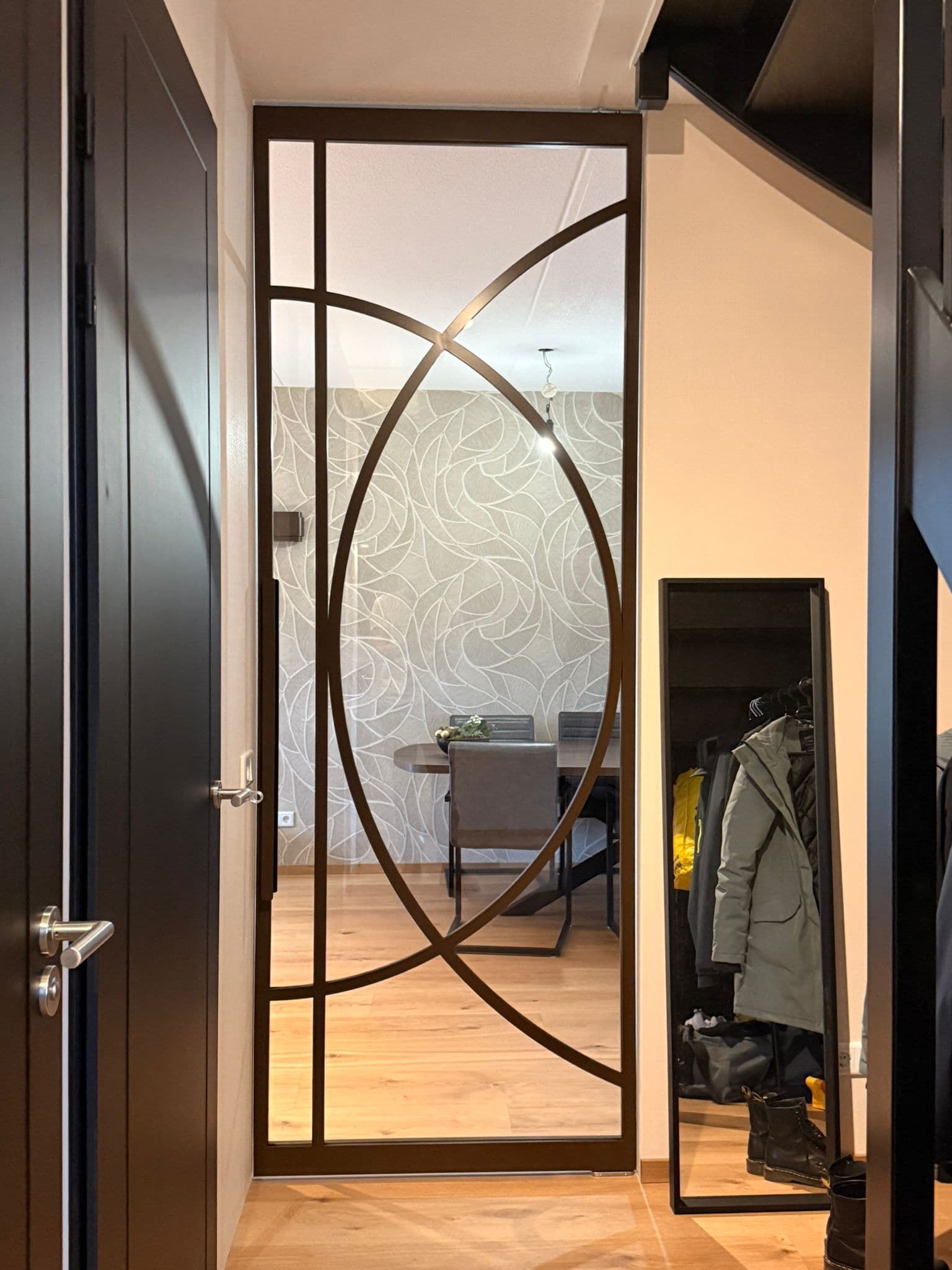 Gesloten kamerhoge bruine stalen taatsdeur met een exclusief organisch boogdesign tussen de hal en de eetkamer.