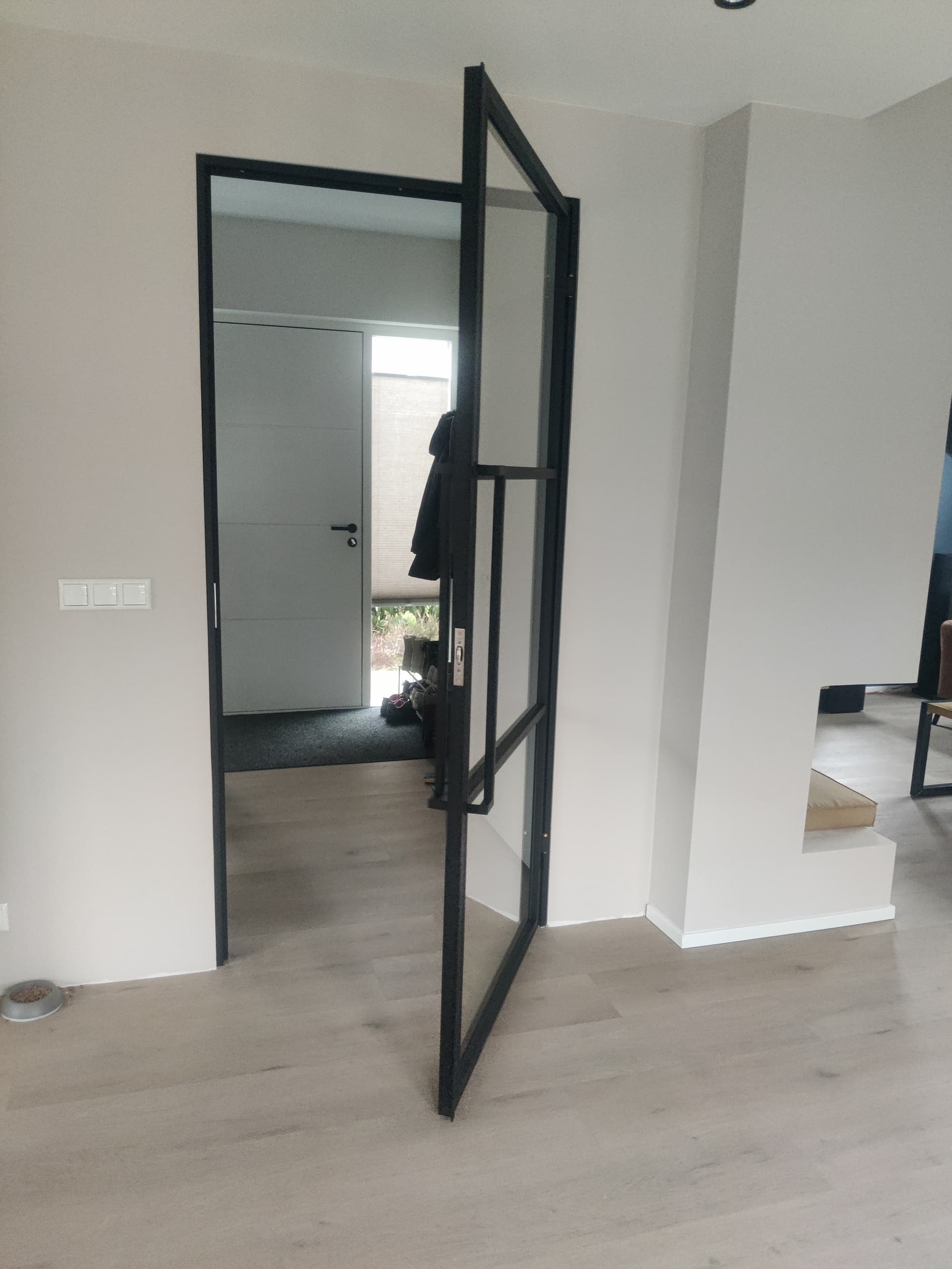 Moderne zwarte stalen binnendeur met helder glas die wijd openstaat in het slanke stalen kozijn.