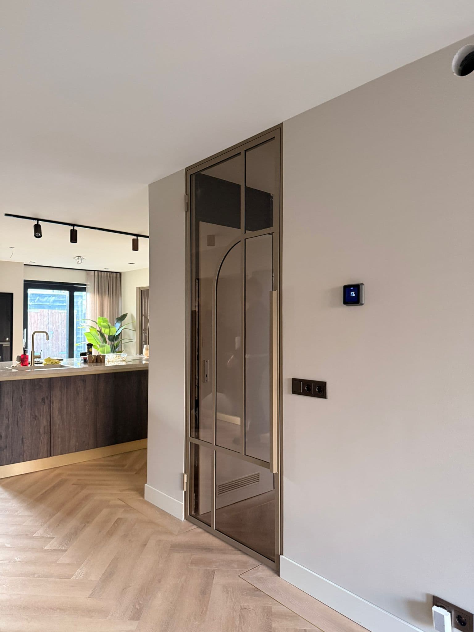 Luxe bruine stalen binnendeur met kozijn en bronskleurig glas, geplaatst naast een moderne houten keuken.
