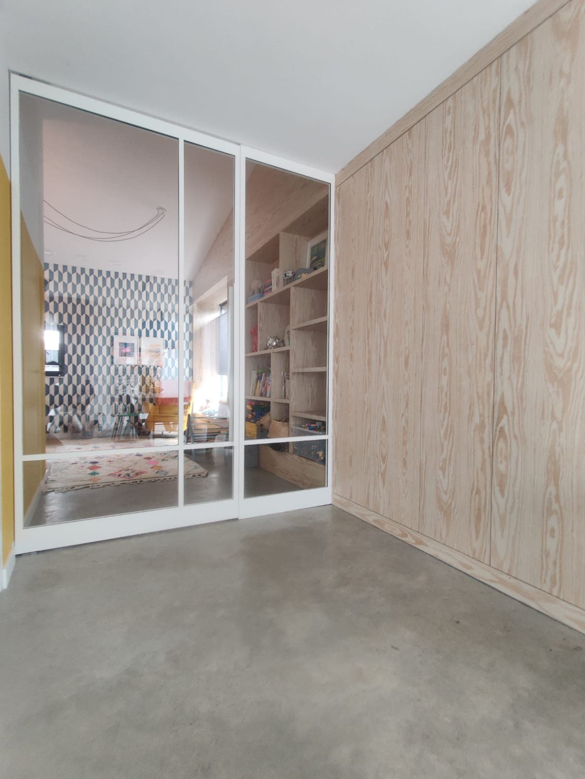 Brede witte stalen taatsdeur op maat met een vast zijpaneel en helder glas in een modern, licht interieur met een betonvloer.