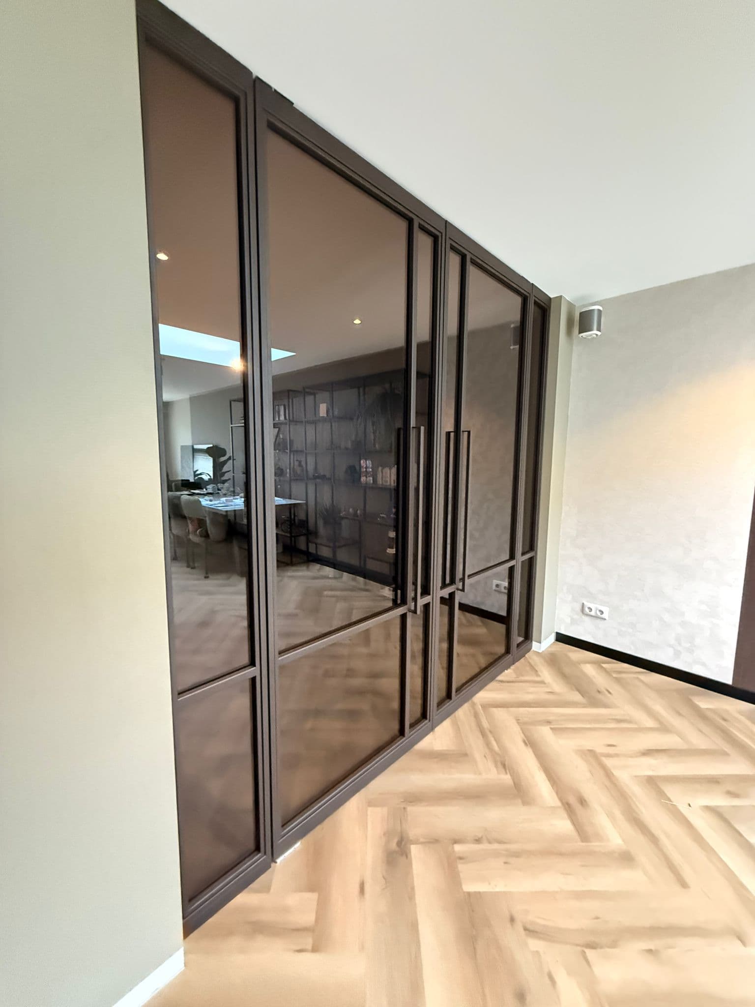 Op maat gemaakte stalen deuren in een chique bruintint met getint veiligheidsglas en strakke verticale handgrepen.