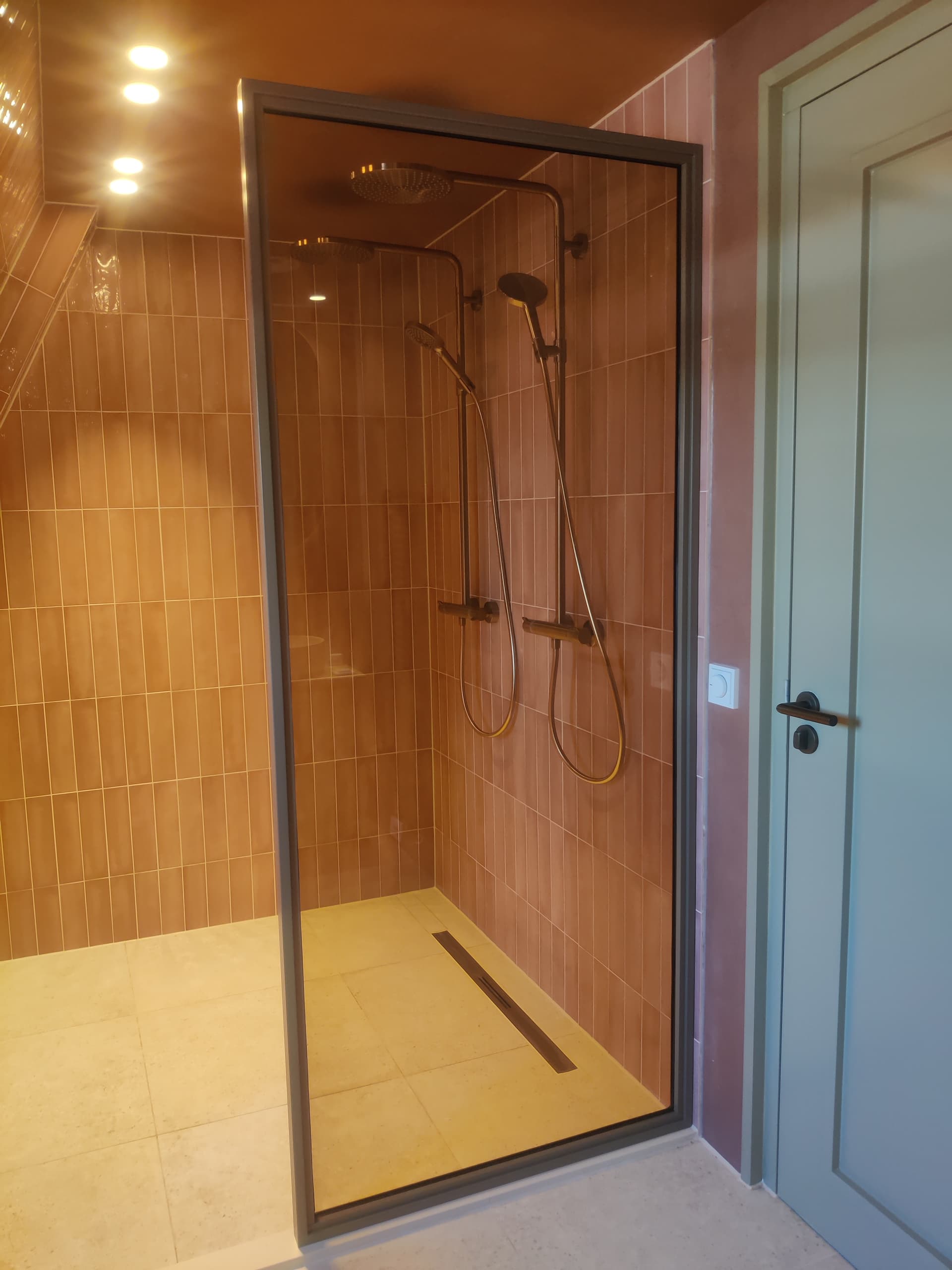 Op maat gemaakte bronzen stalen douchewand als los vast paneel voor een moderne inloopdouche met terracotta tegels.