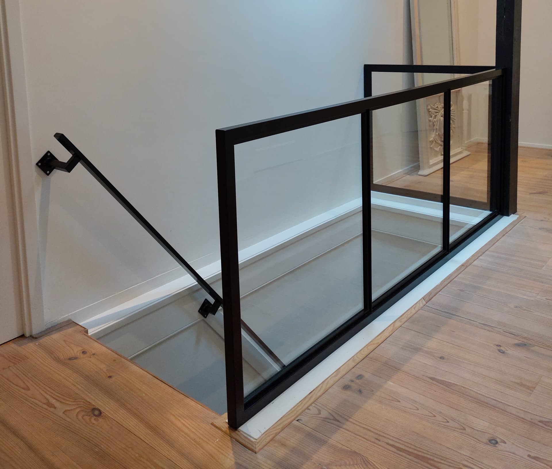 Zwarte stalen balustrade met glas rond een trapgat, met een bijpassende muurleuning langs de trap.