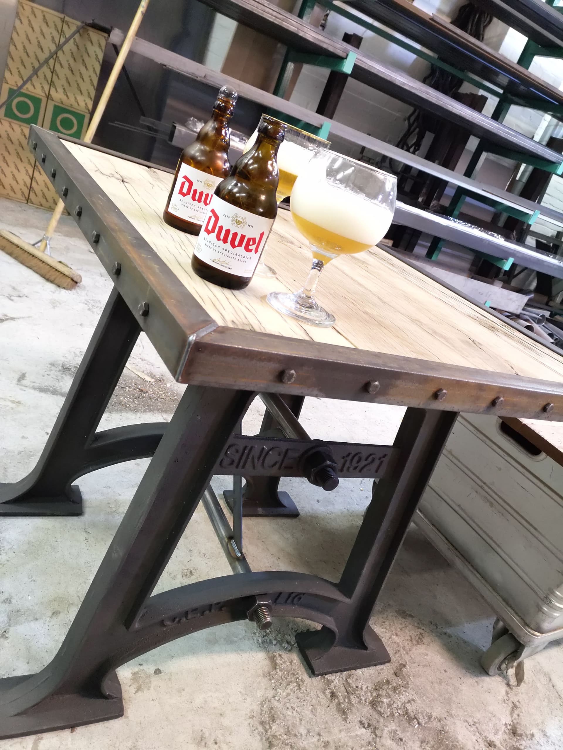 Industriële tafel met houten blad op een gietijzeren onderstel met het opschrift Since 1921, in de werkplaats.