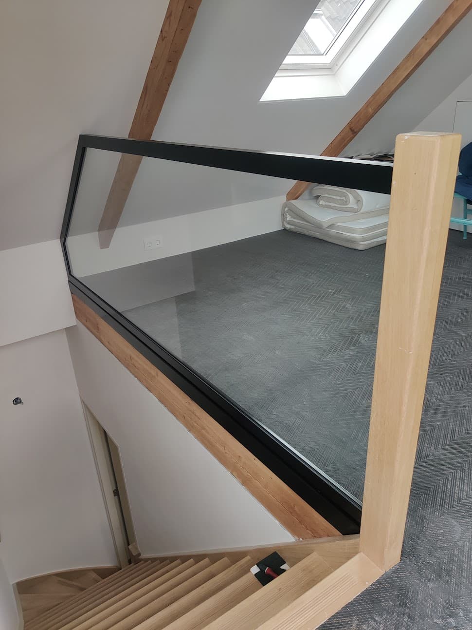 Stalen balustrade met glas rond een trapgat op zolder, met een profiel dat met de trap mee naar beneden loopt.