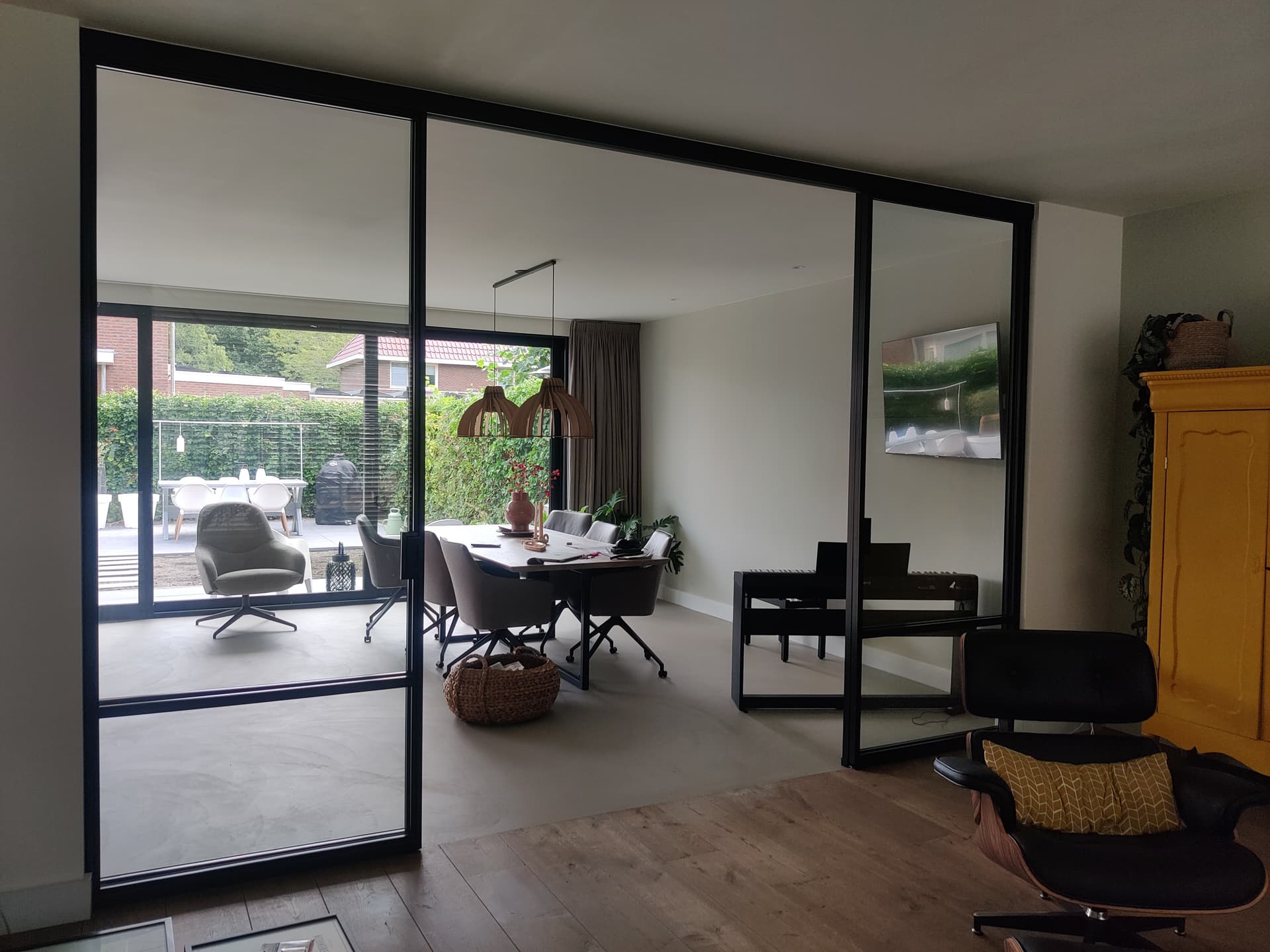 Zwarte stalen binnenpui met schuifdeuren over de volle breedte, met zicht op een eetkamer en de tuin daarachter.