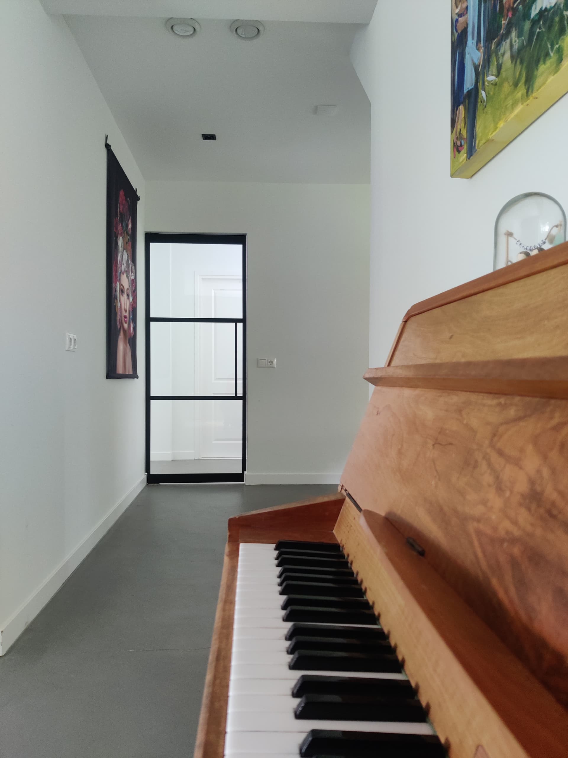Smalle zwarte stalen taatsdeur met matglas aan het eind van een gang, met een piano op de voorgrond.