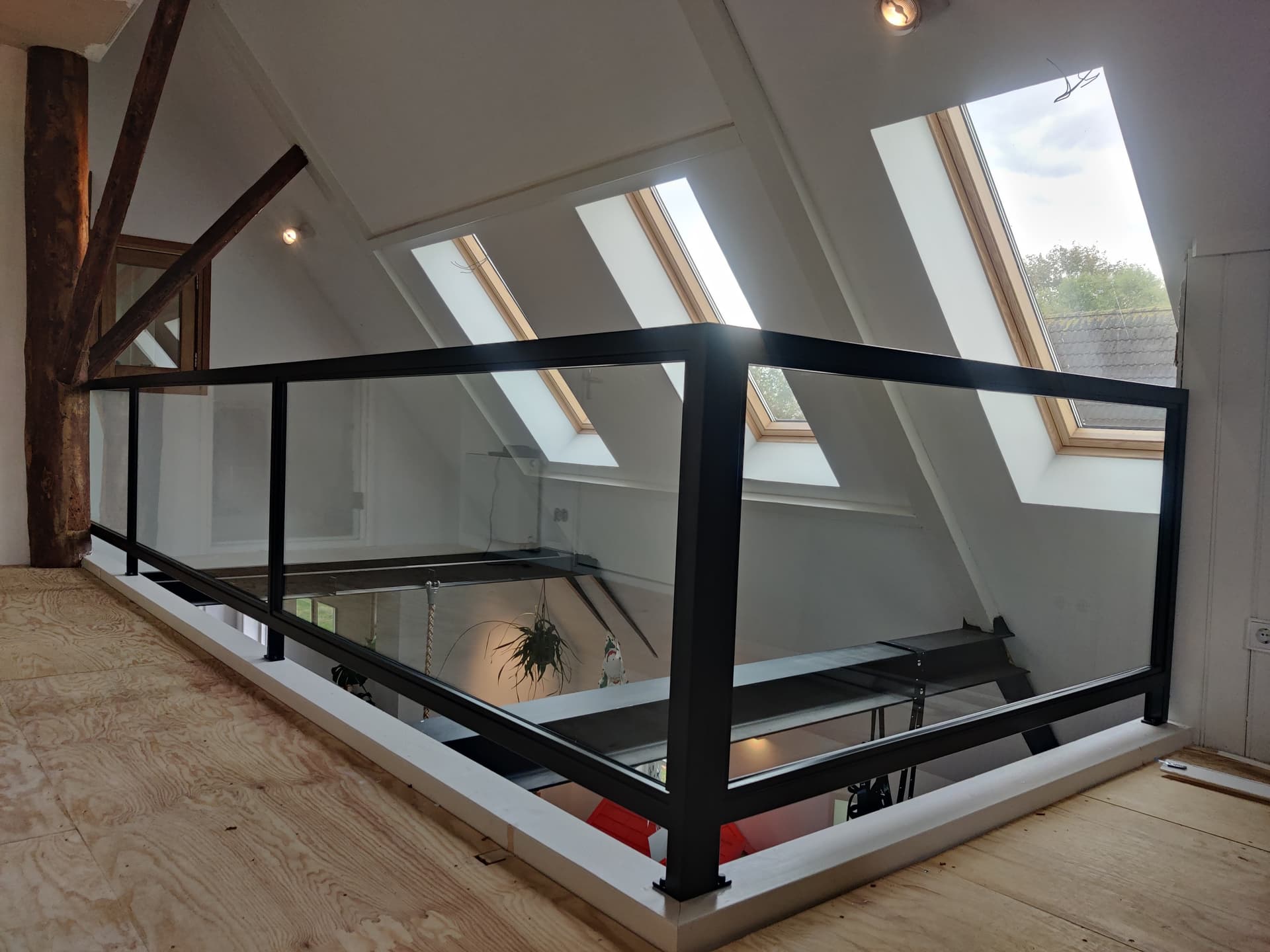 Zwarte stalen balustrade met glas langs een vide onder een schuin dak met dakramen.