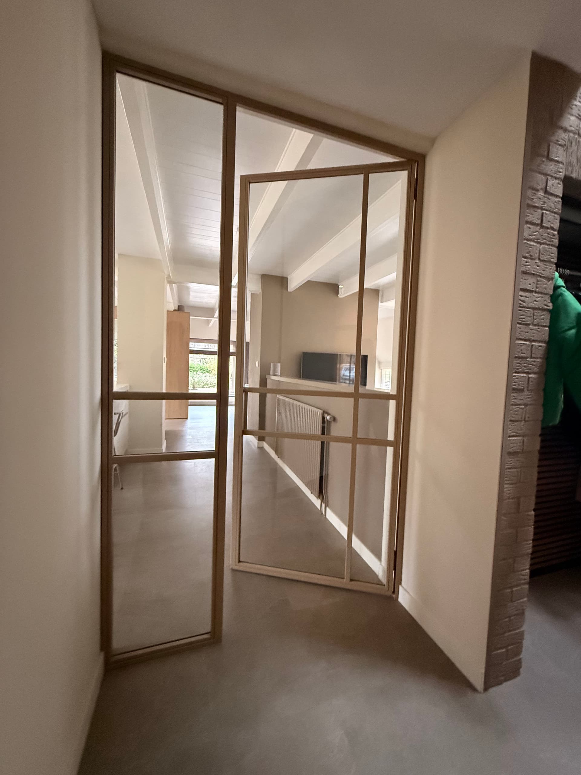 Op maat gemaakte zandkleurige stalen binnenpui met helder veiligheidsglas en een moderne, asymmetrische vakverdeling.