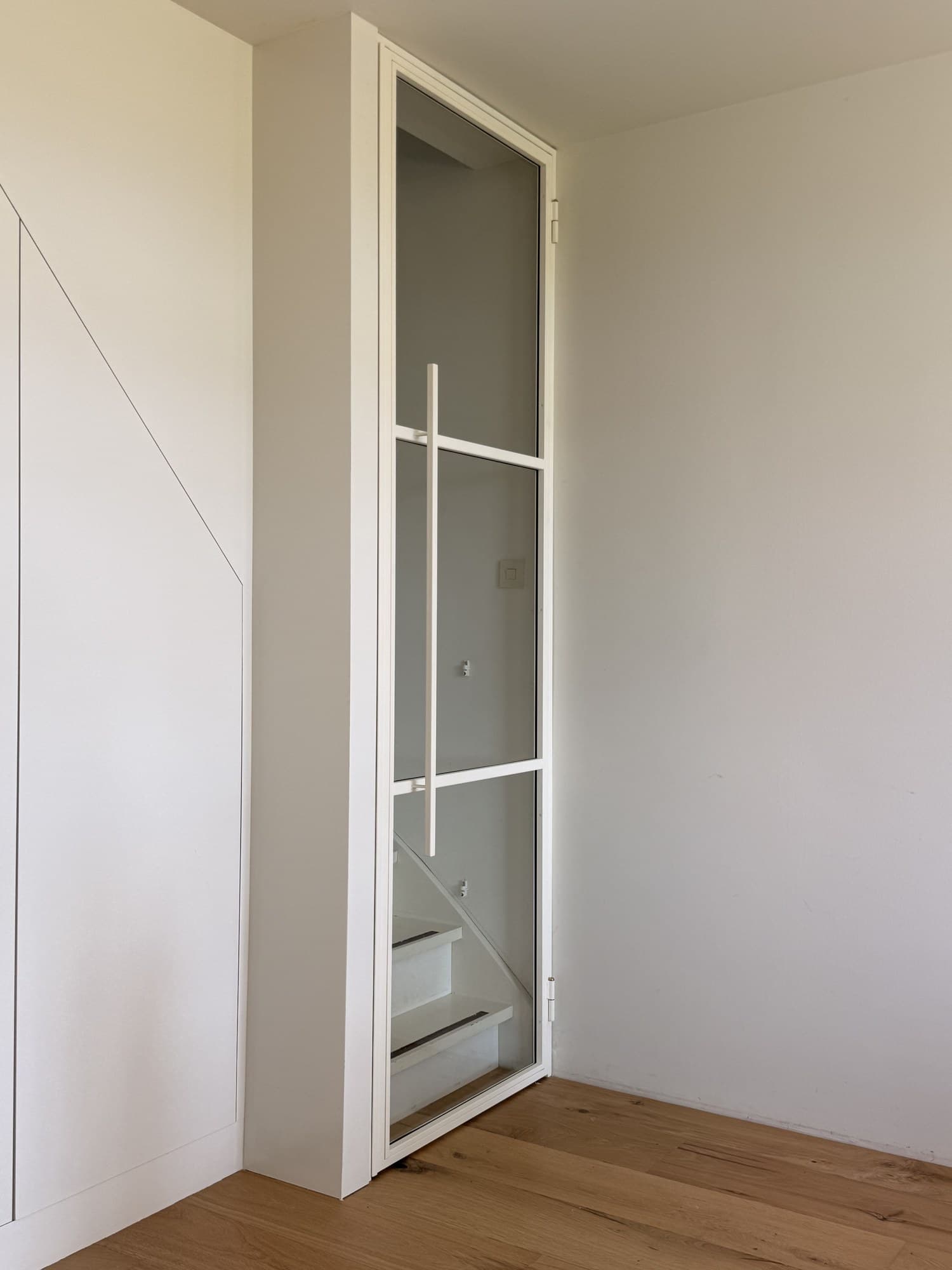 Witte stalen scharnierdeur half geopend, met het slanke kozijn en de scharnieren in beeld.