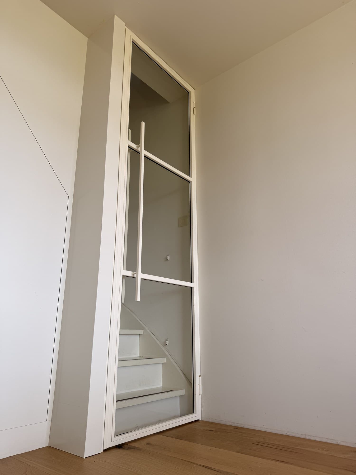 Witte stalen scharnierdeur op een kier, gezien vanuit de woonkamer richting de trap.