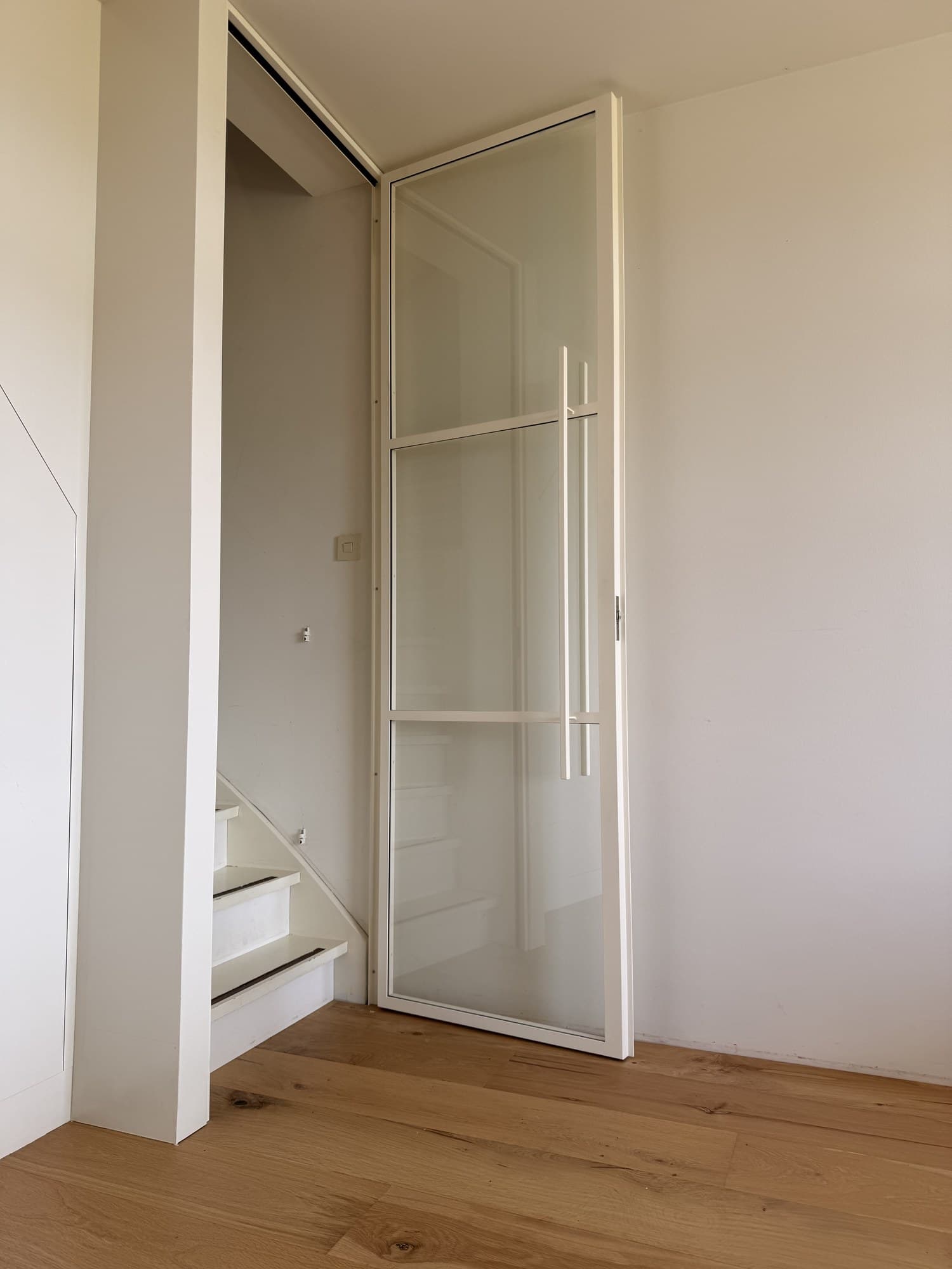 Witte stalen scharnierdeur helemaal geopend, met de lange verticale greep.