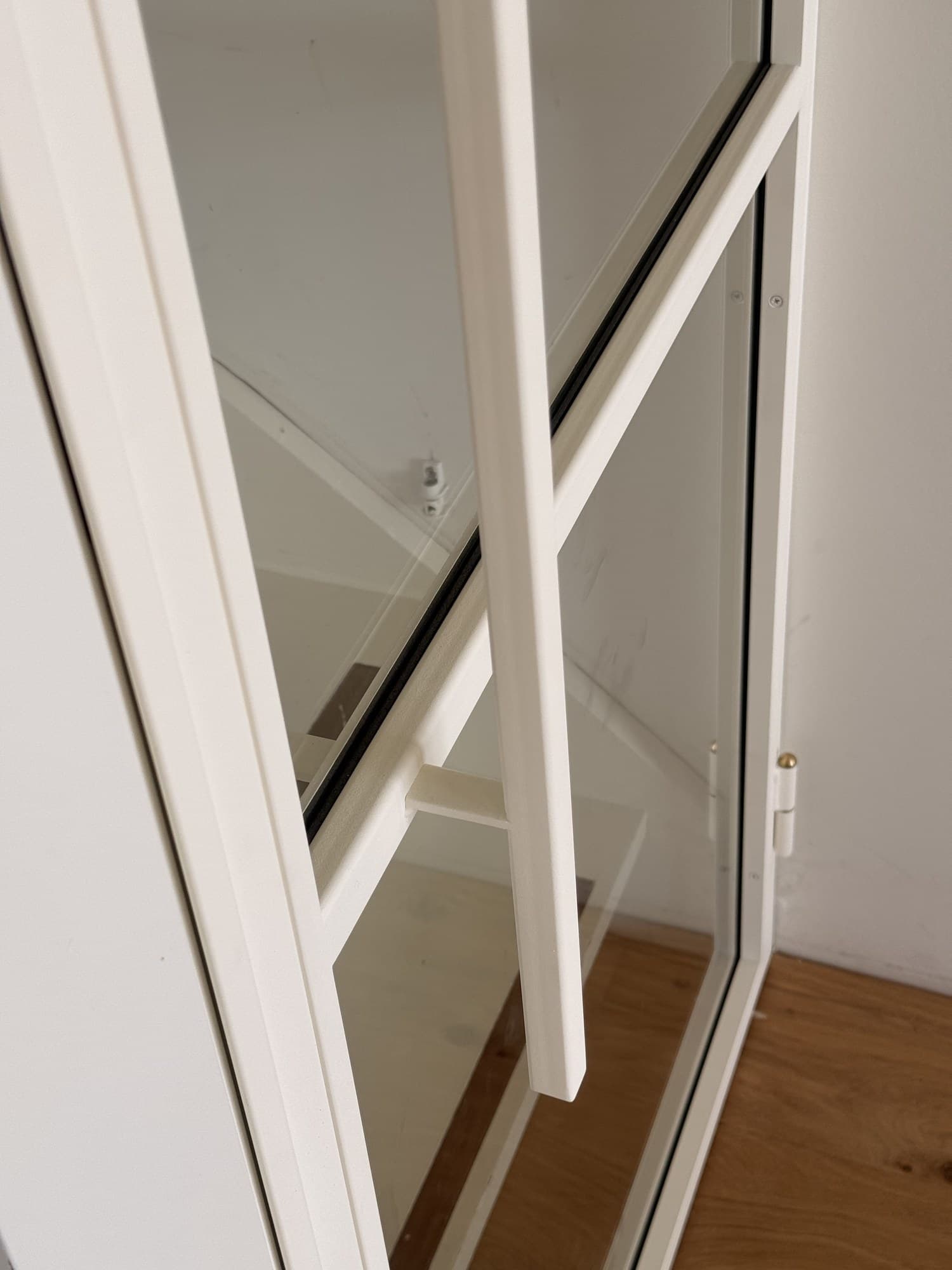 Detailopname van het slanke witte stalen profiel en het glas van de scharnierdeur.