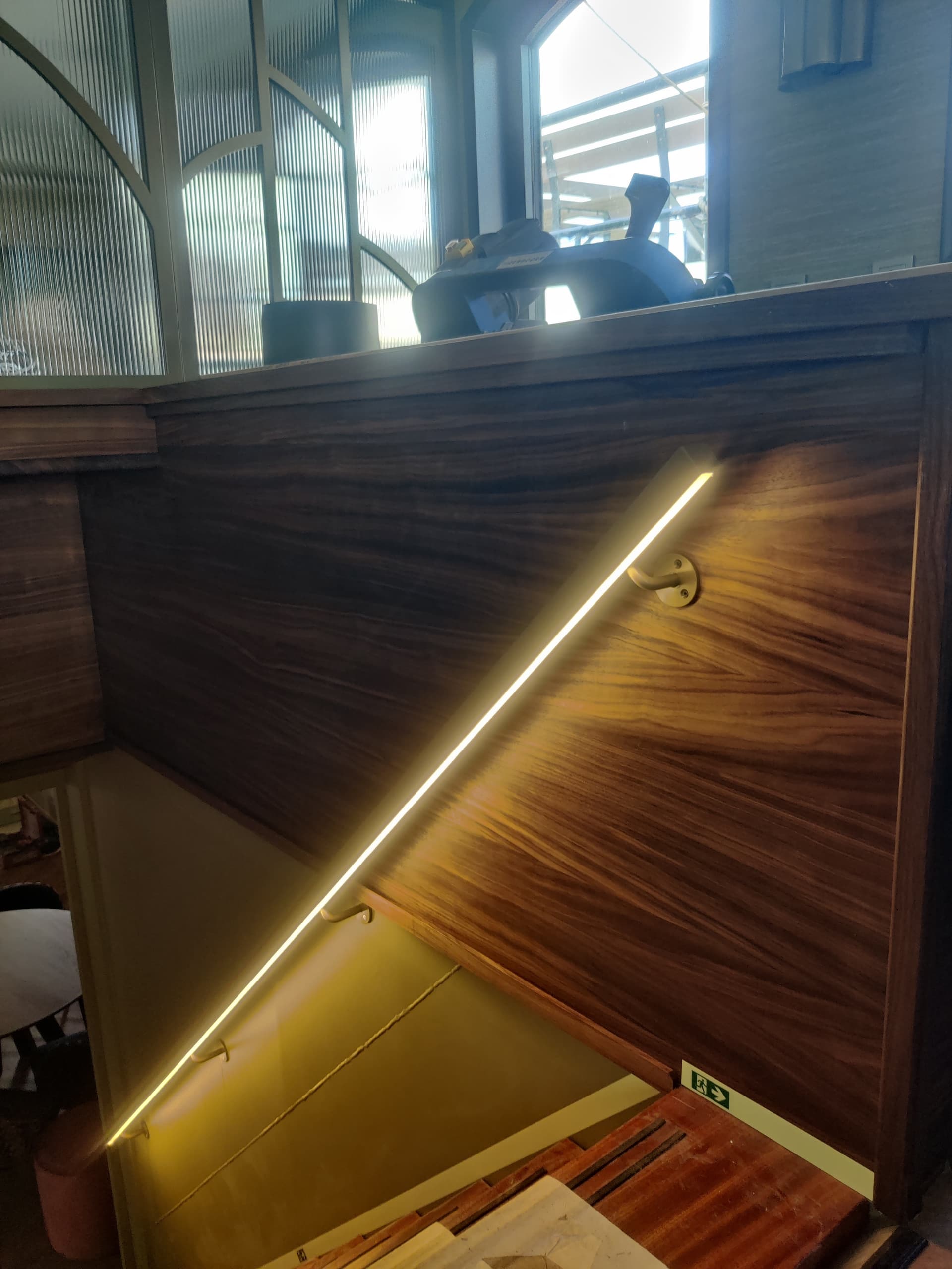 Stalen trapleuning met doorlopende ledverlichting langs een houten wandbetimmering, aan boord van een schip.