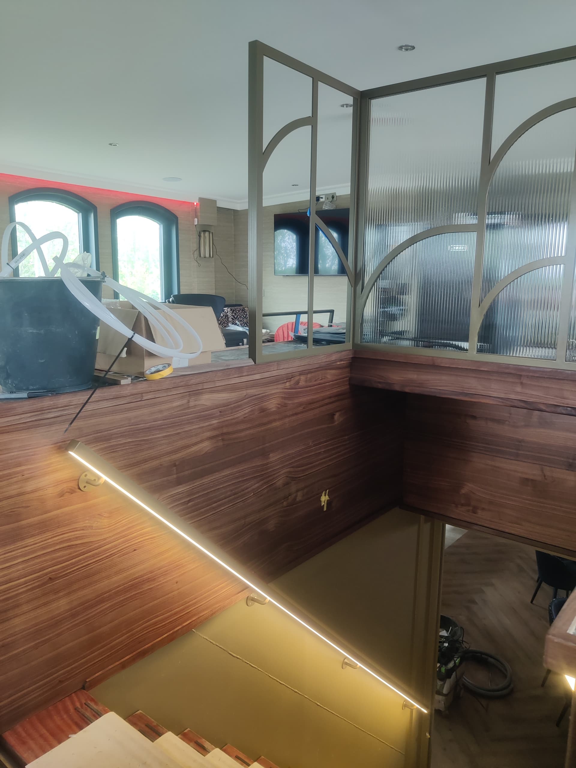 Goudkleurige stalen roomdivider met geribbeld glas en boogmotief boven een houten wandbetimmering, aan boord van een schip.
