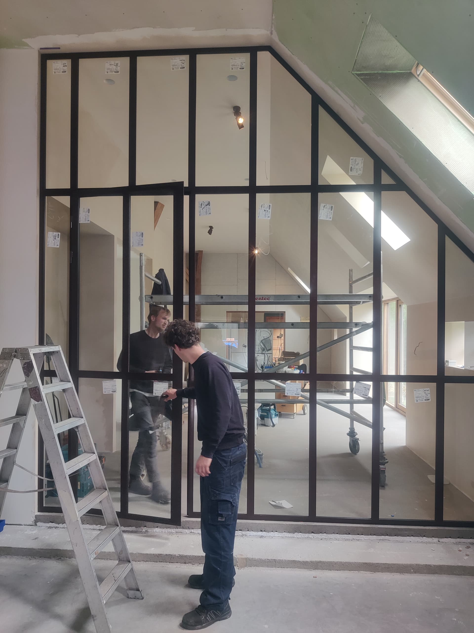 Twee monteurs plaatsen het glas in een grote stalen scheidingswand met deur, in een woning in aanbouw.