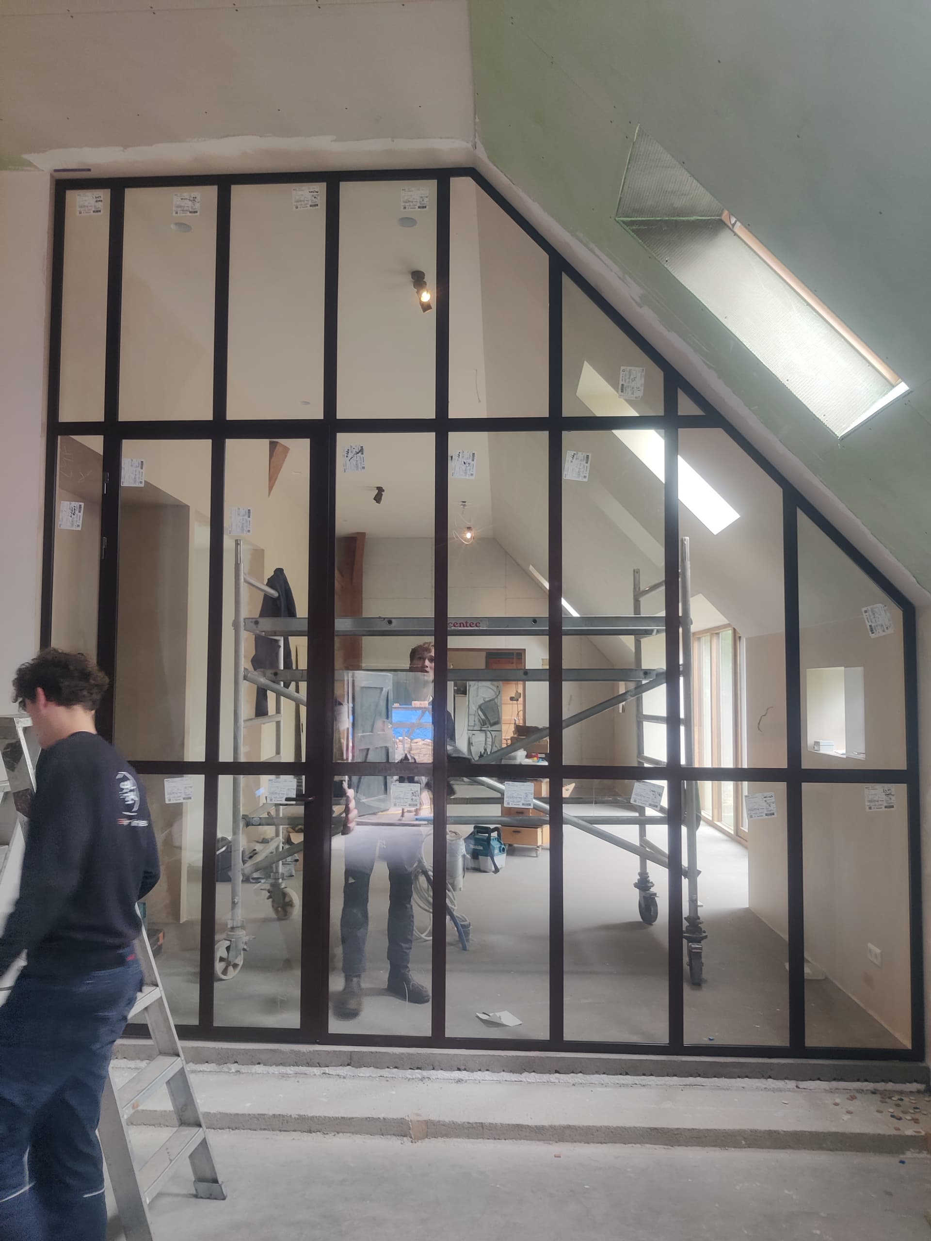 Monteurs bij een grote stalen scheidingswand met deur, nog voorzien van montagestickers op het glas.