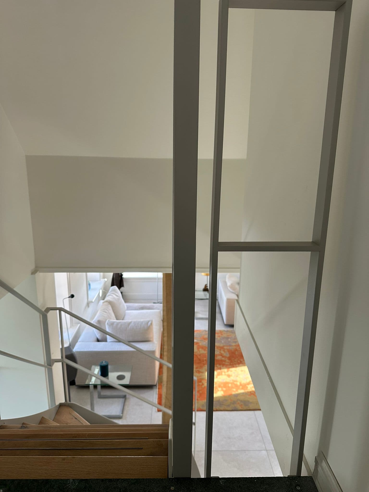 Lichtgrijze stalen balustrade langs een vide, met zicht op de woonkamer beneden.