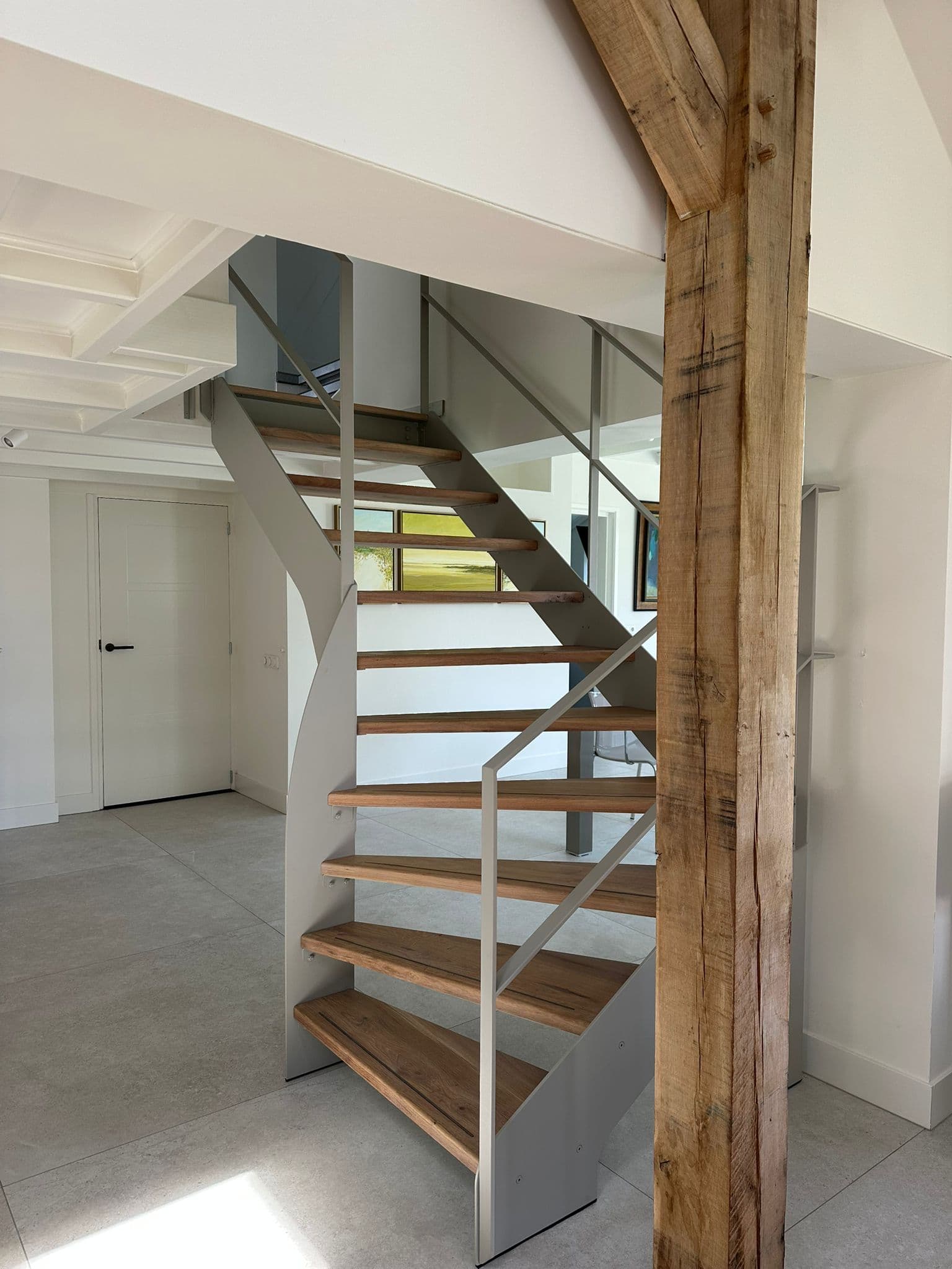 Moderne open stalen trap met een lichtgrijze coating, massief eikenhouten treden en een minimalistische stalen balustrade.