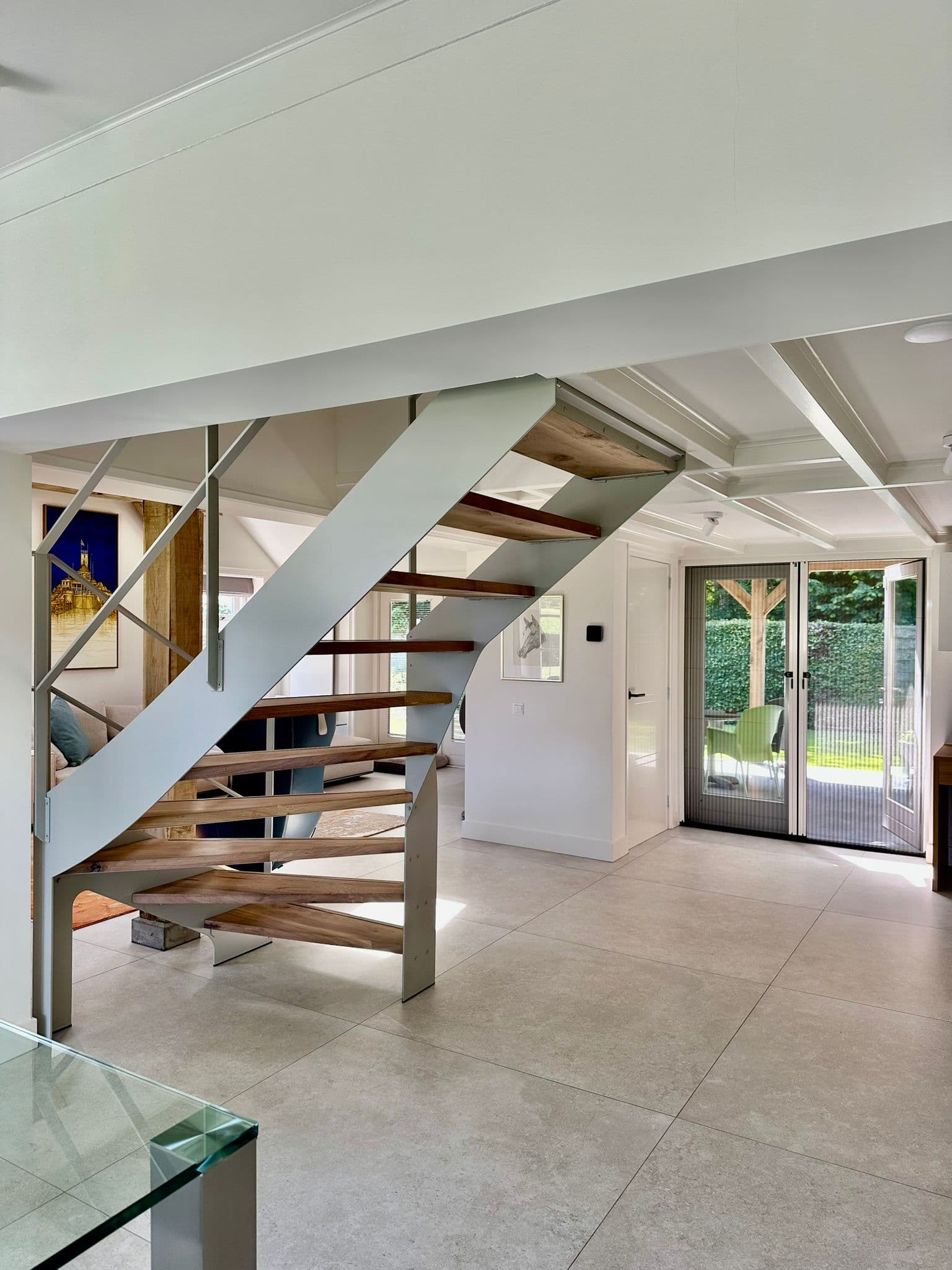 Open stalen designtrap met lichtgrijze coating en eikenhouten treden, zwevend in een lichte woonkamer.