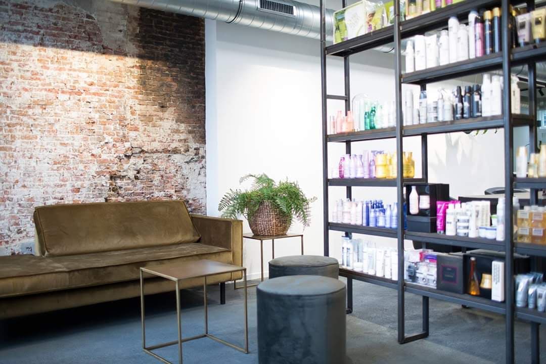 Hoge stalen stellingkast met producten langs een muur van oud metselwerk, in een kapsalon met leren bank.
