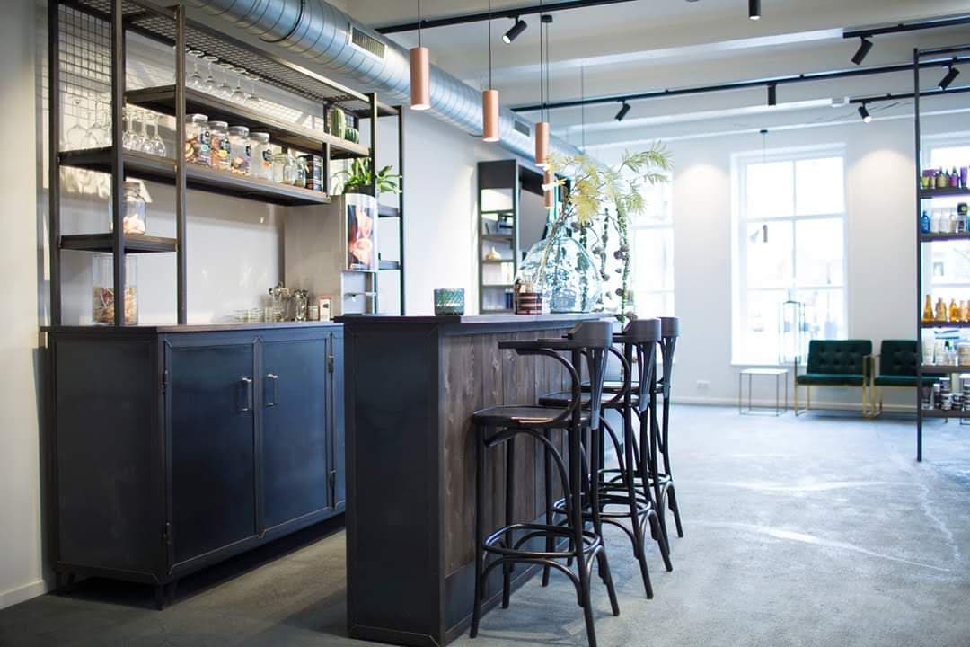 Stalen stellingkast met open vakken en dichte onderkasten achter een bar met houten blad, in een horecazaak met betonvloer.