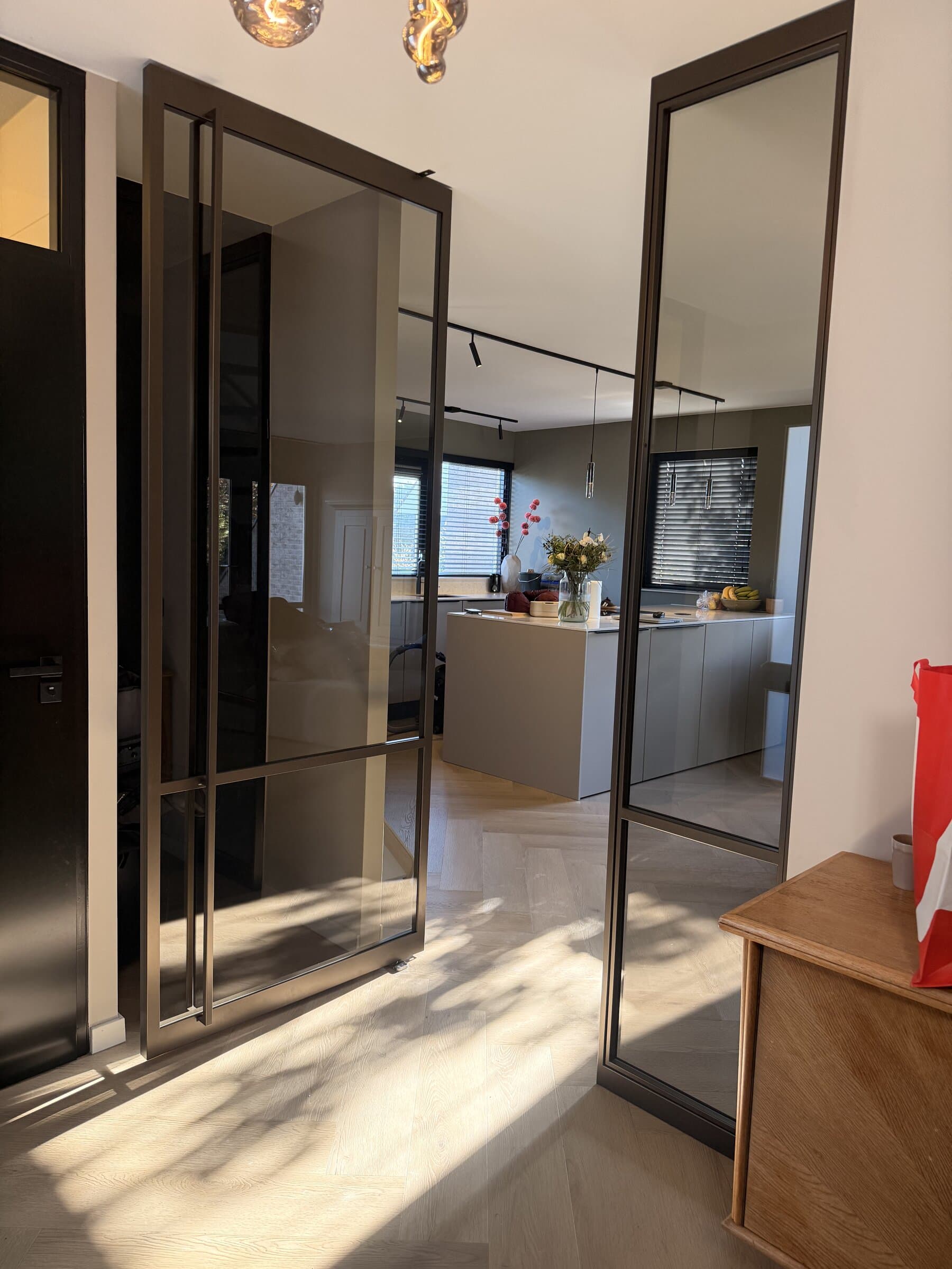 Geopende stalen taatsdeur met zijlicht in anodic brown, met door de opening zicht op de keuken en de woonkamer.