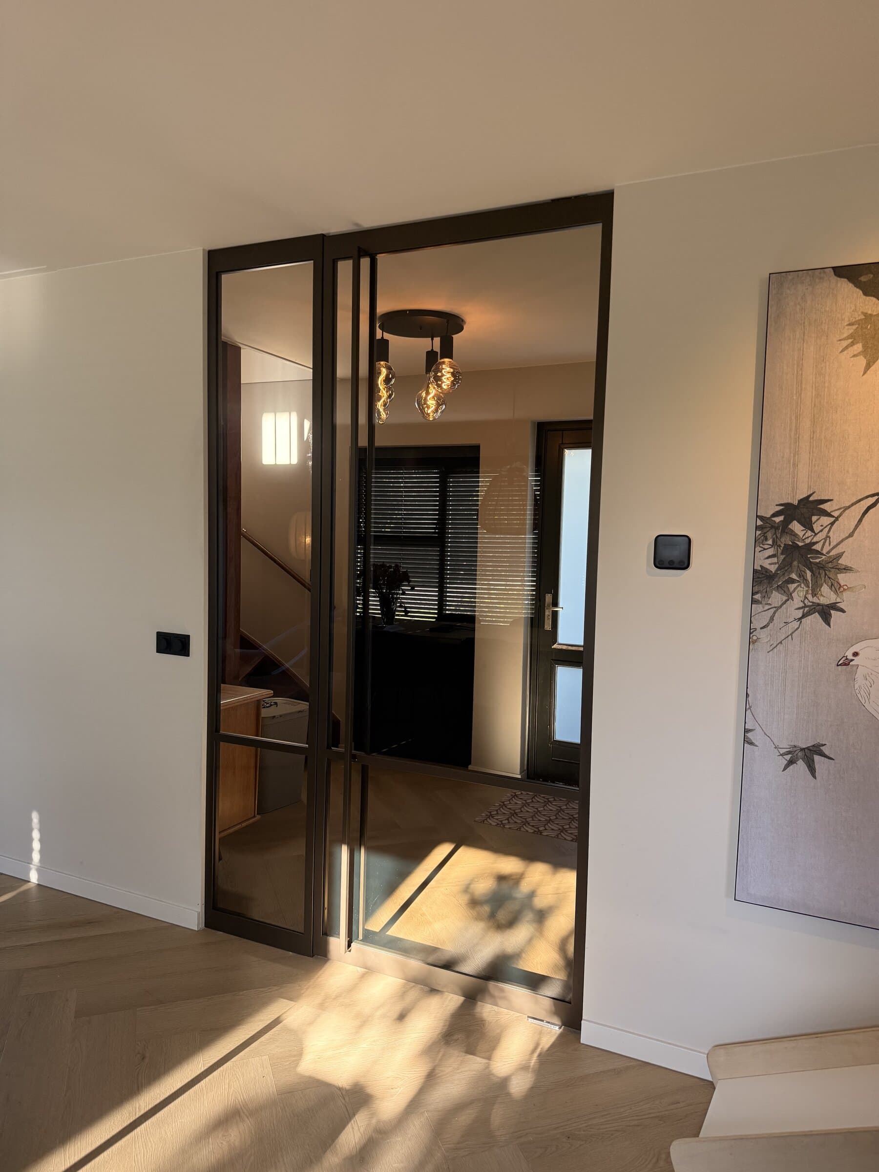 Stalen taatsdeur met zijlicht in anodic brown, gesloten, gezien vanuit de woonkamer naar de hal met de trap.