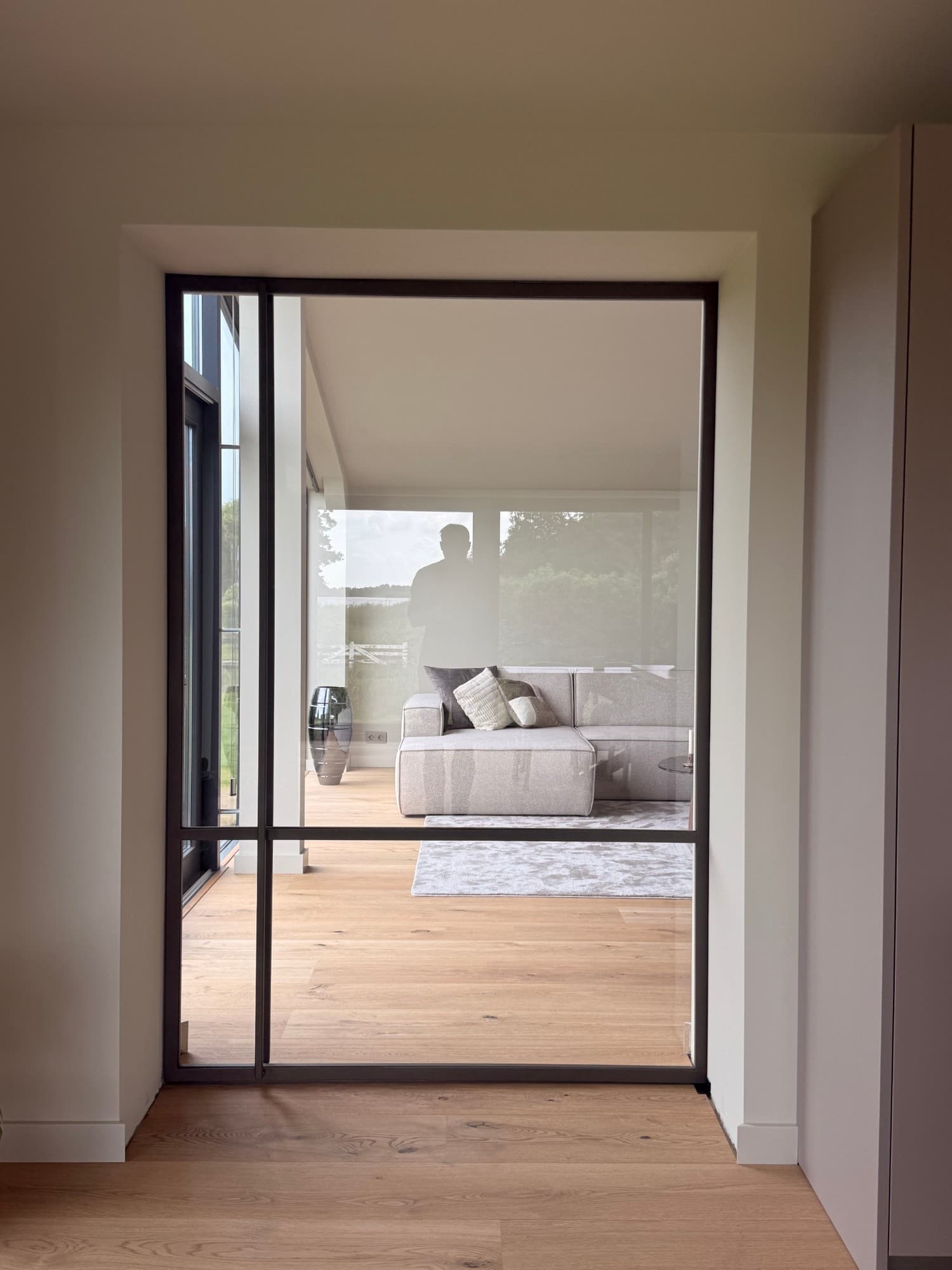 Brede bruine stalen schuifdeur recht van voren, met de slanke profielen, de dwarsregel en zicht door het glas op de woonkamer.