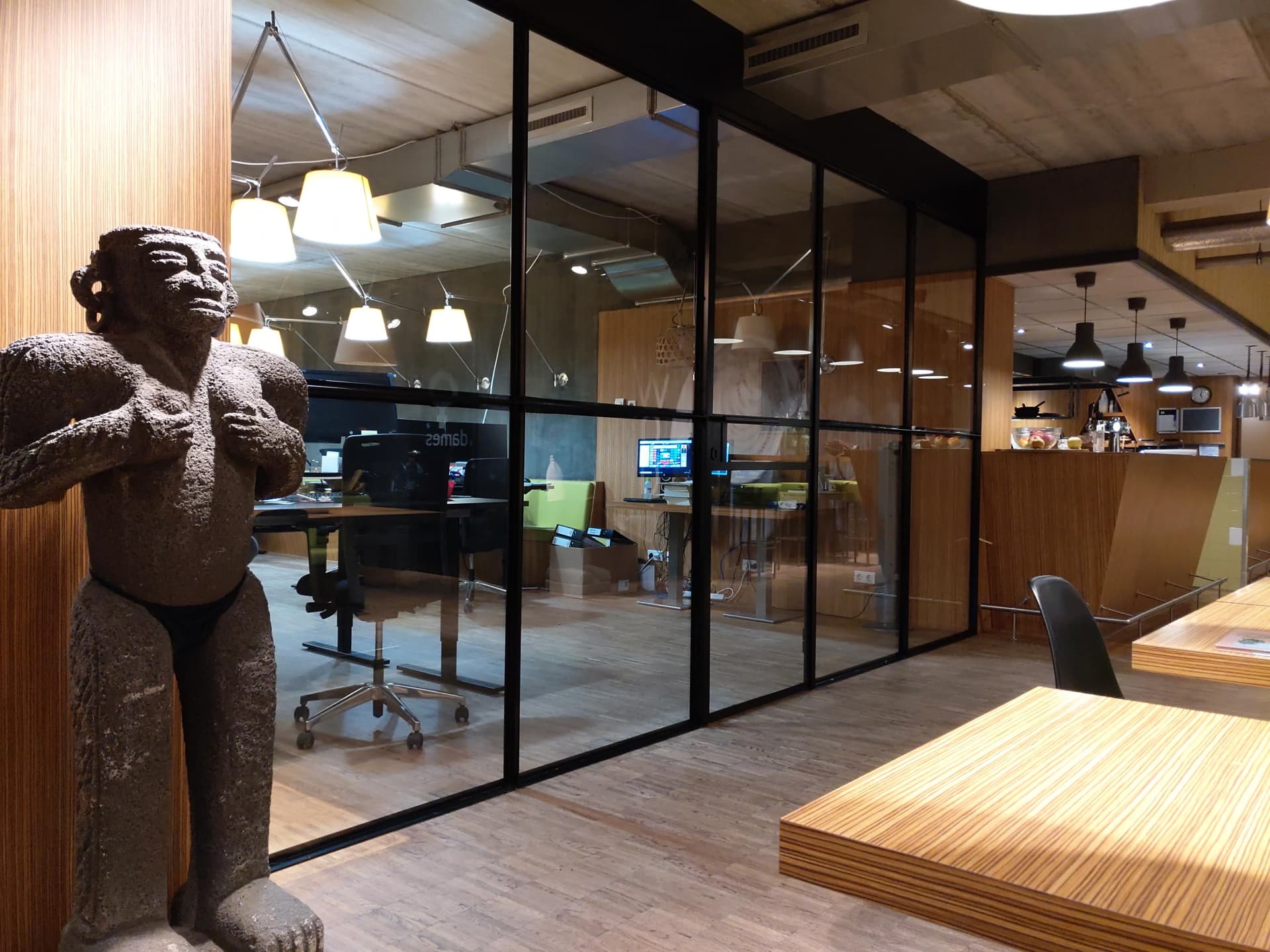 Zwarte stalen scheidingswand met glas tussen een kantoorruimte en een gang, in een bedrijfspand met houten wanden.