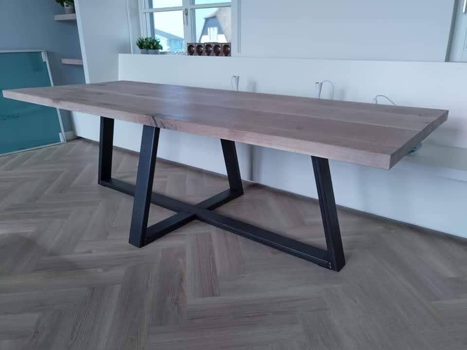 Houten eettafel op een zwart stalen onderstel met schuine poten en kruisverbinding, op een visgraatvloer.