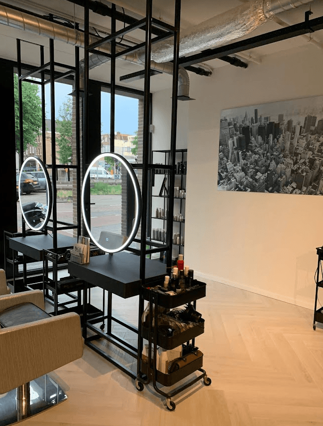 Stalen kapperselementen met ronde verlichte spiegels en open rekken, als roomdivider midden in een kapsalon.