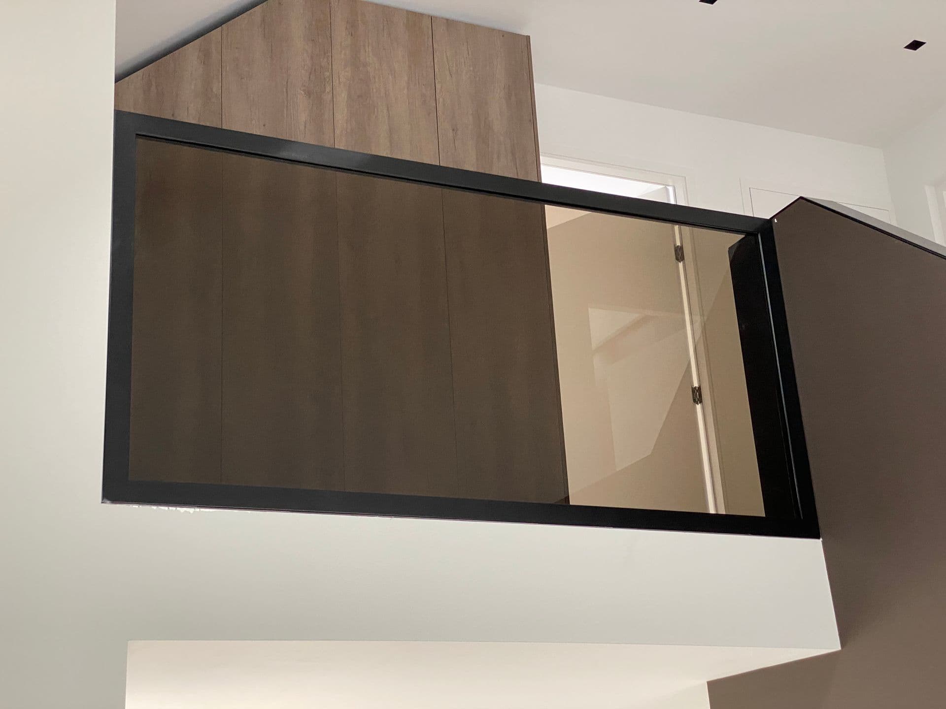 Stalen balustrade met brons getint glas langs een vide, met een houten wand op de achtergrond.