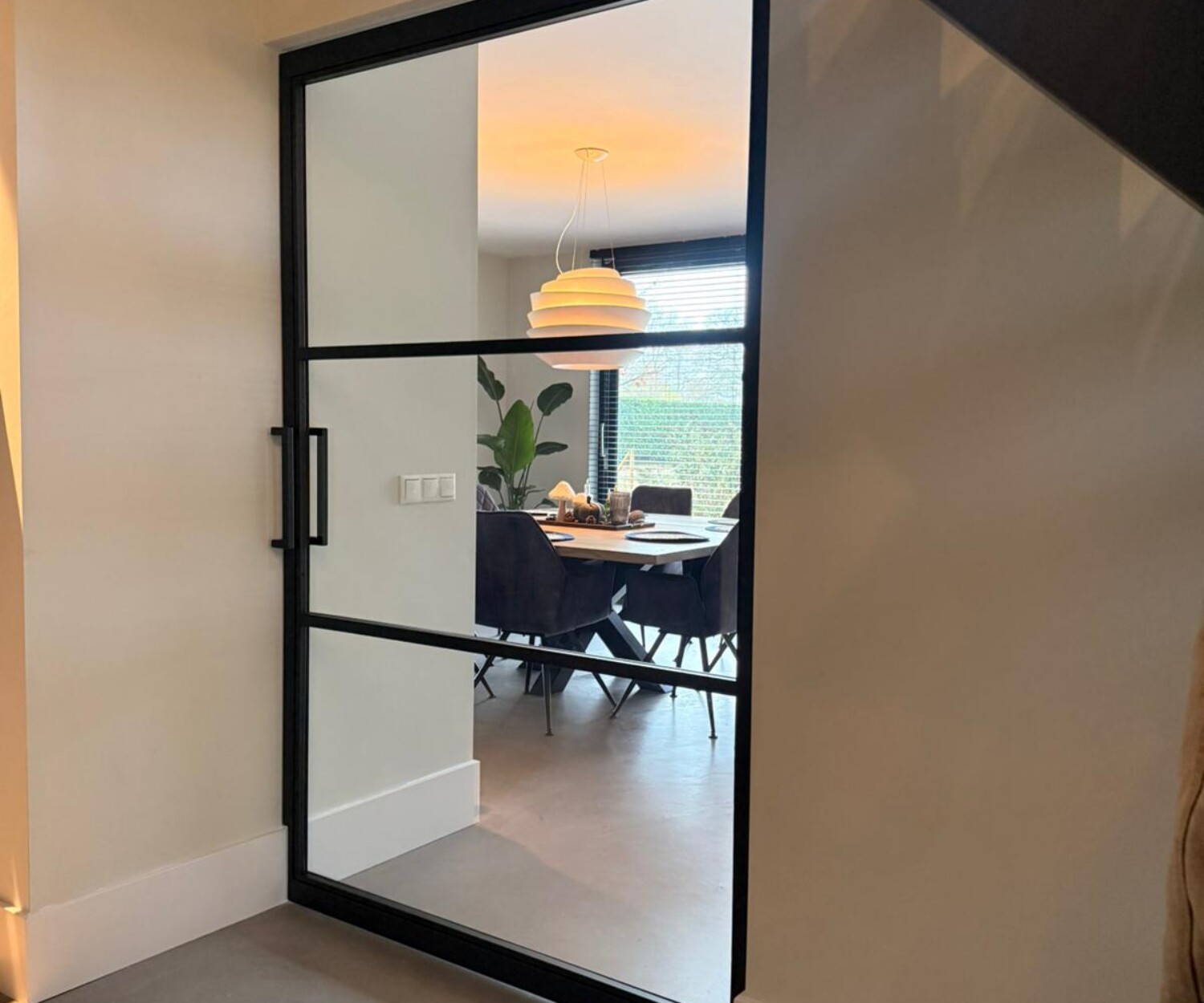 Brede stalen taatsdeur op maat met een moderne 3-vaks verdeling en helder glas tussen de hal en de lichte woonkeuken.