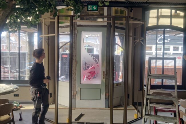 Montage van een goudkleurige stalen tochtsluis op maat rondom de café-entree om tocht in de horeca tegen te gaan.