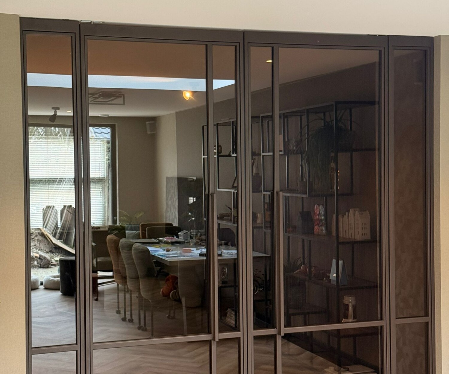 Kamerhoge bruine stalen pui met dubbele openslaande deuren, vaste zijpanelen en getint glas in een luxe interieur met visgraatvloer.