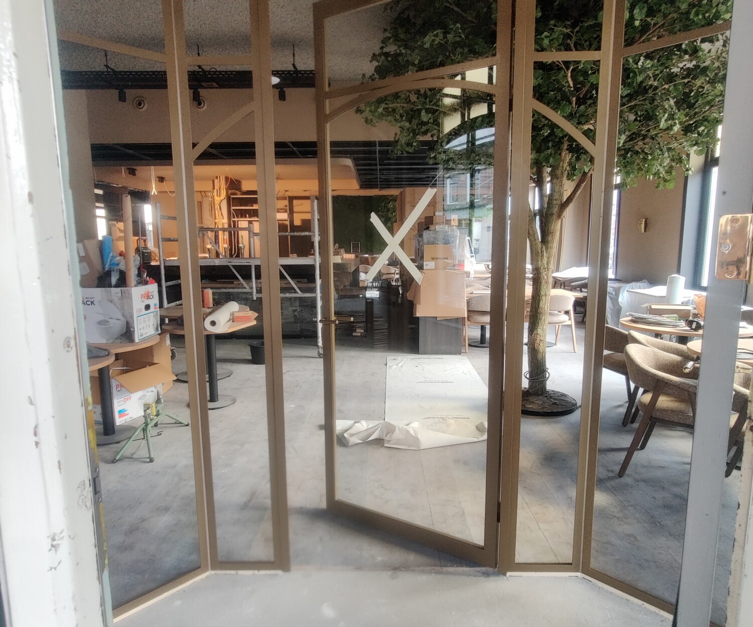 Op maat gemaakte goudkleurige stalen tochtsluis met een geopende binnendeur en helder glas in het interieur van een sfeervol café.