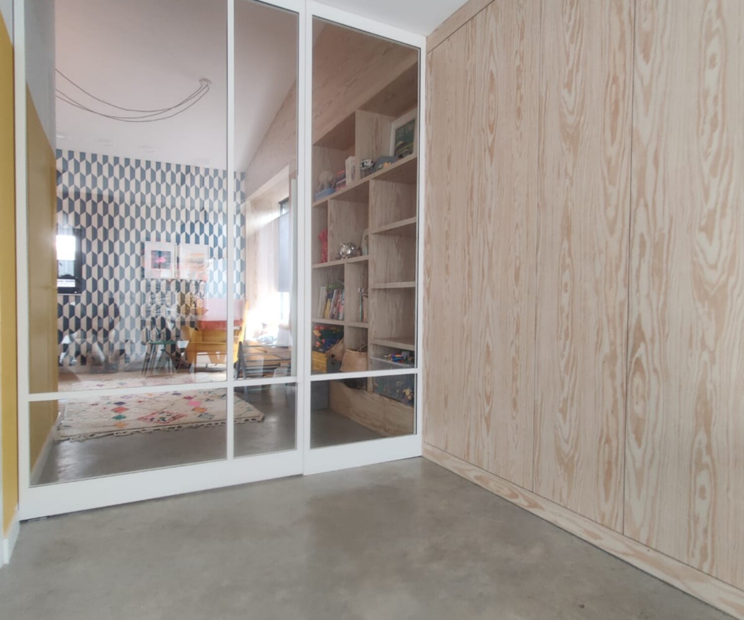 Brede witte stalen taatsdeur op maat met een vast zijpaneel en helder glas in een modern, licht interieur met een betonvloer.