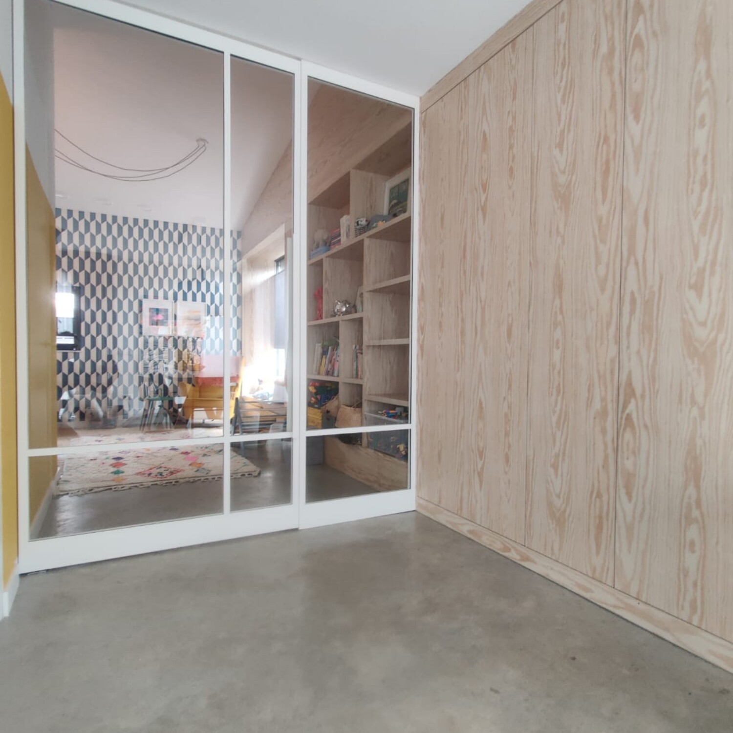 Brede witte stalen taatsdeur op maat met een vast zijpaneel en helder glas in een modern, licht interieur met een betonvloer.