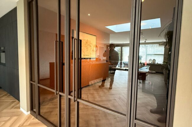 Luxe vierdelige stalen binnenpui in een warme bruine coating met sfeervol getint glas, gezien vanuit de open keuken.