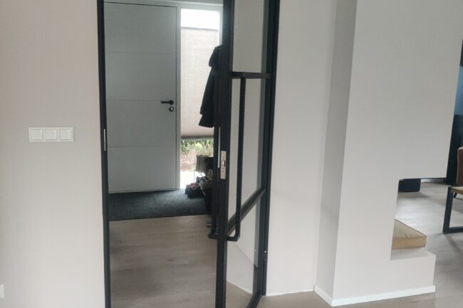 Moderne zwarte stalen binnendeur met helder glas die wijd openstaat in het slanke stalen kozijn.