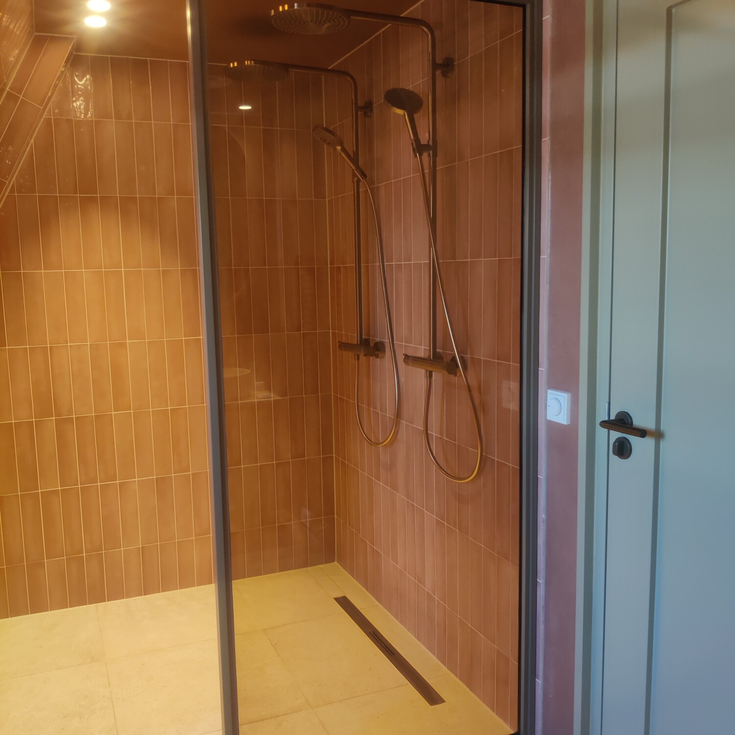Op maat gemaakte bronzen stalen douchewand als los vast paneel voor een moderne inloopdouche met terracotta tegels.