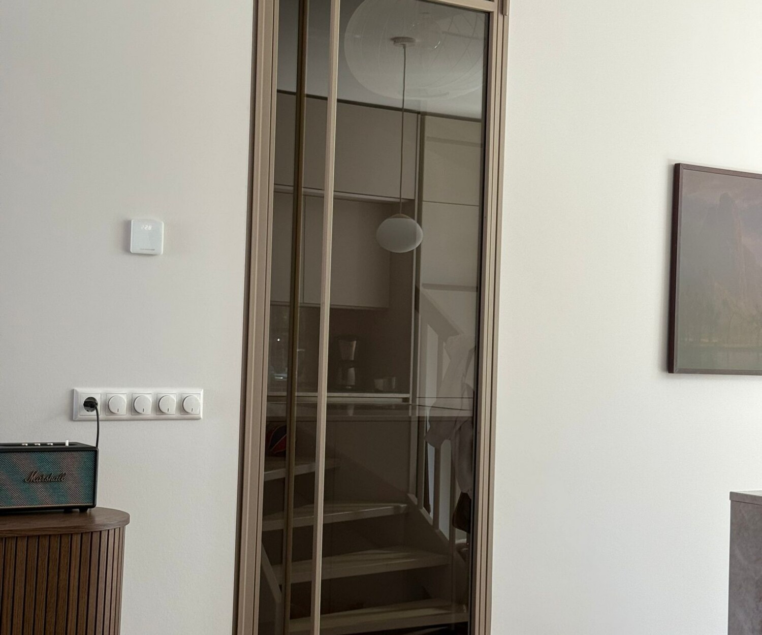 Elegante bronzen stalen scharnierdeur in kozijn met brons getint glas en een lange verticale handgreep in een modern interieur met visgraatvloer