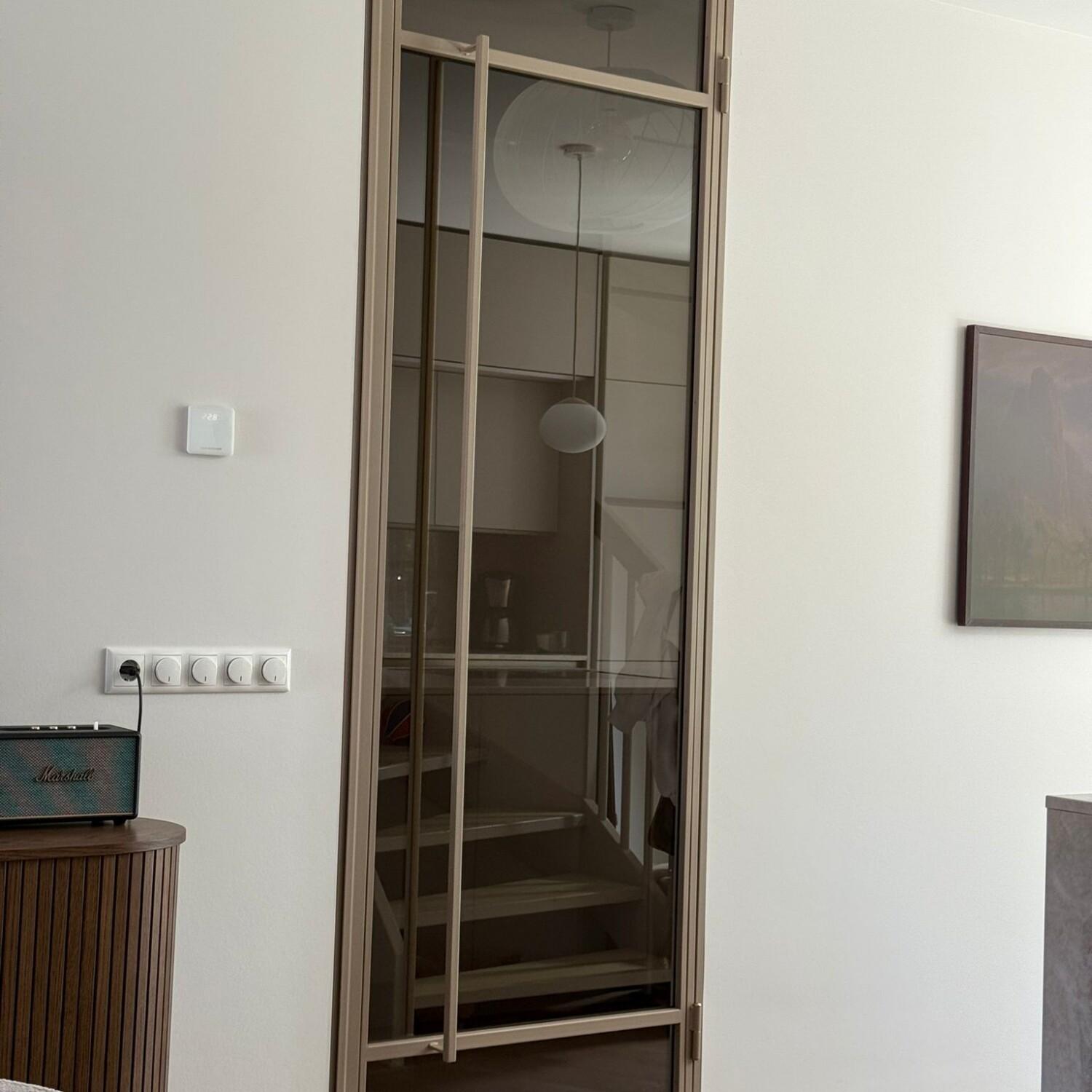 Elegante bronzen stalen scharnierdeur in kozijn met brons getint glas en een lange verticale handgreep in een modern interieur met visgraatvloer