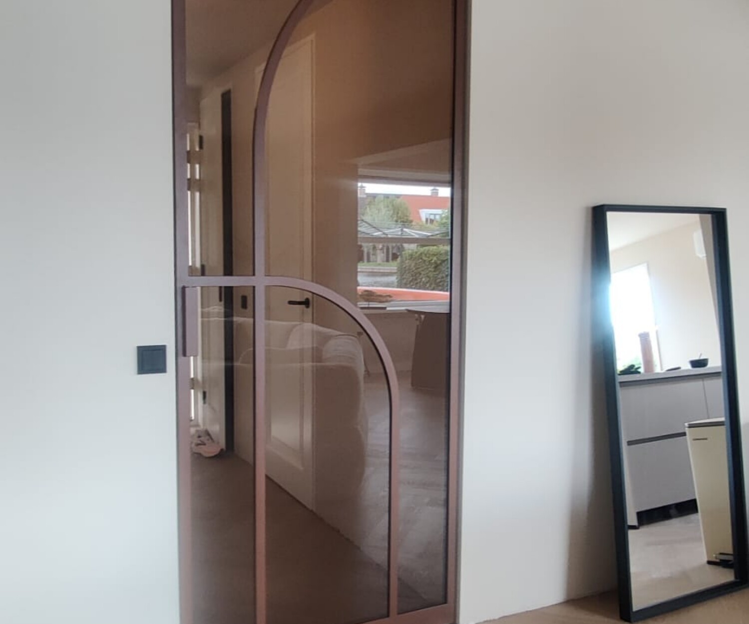 Enkele bronzen stalen deur met een asymmetrisch boogontwerp en brons getint glas in een modern interieur met visgraatvloer.