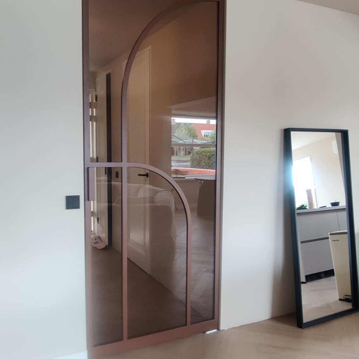Enkele bronzen stalen deur met een asymmetrisch boogontwerp en brons getint glas in een modern interieur met visgraatvloer.
