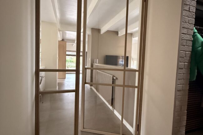 Op maat gemaakte zandkleurige stalen binnenpui met helder veiligheidsglas en een moderne, asymmetrische vlakverdeling.